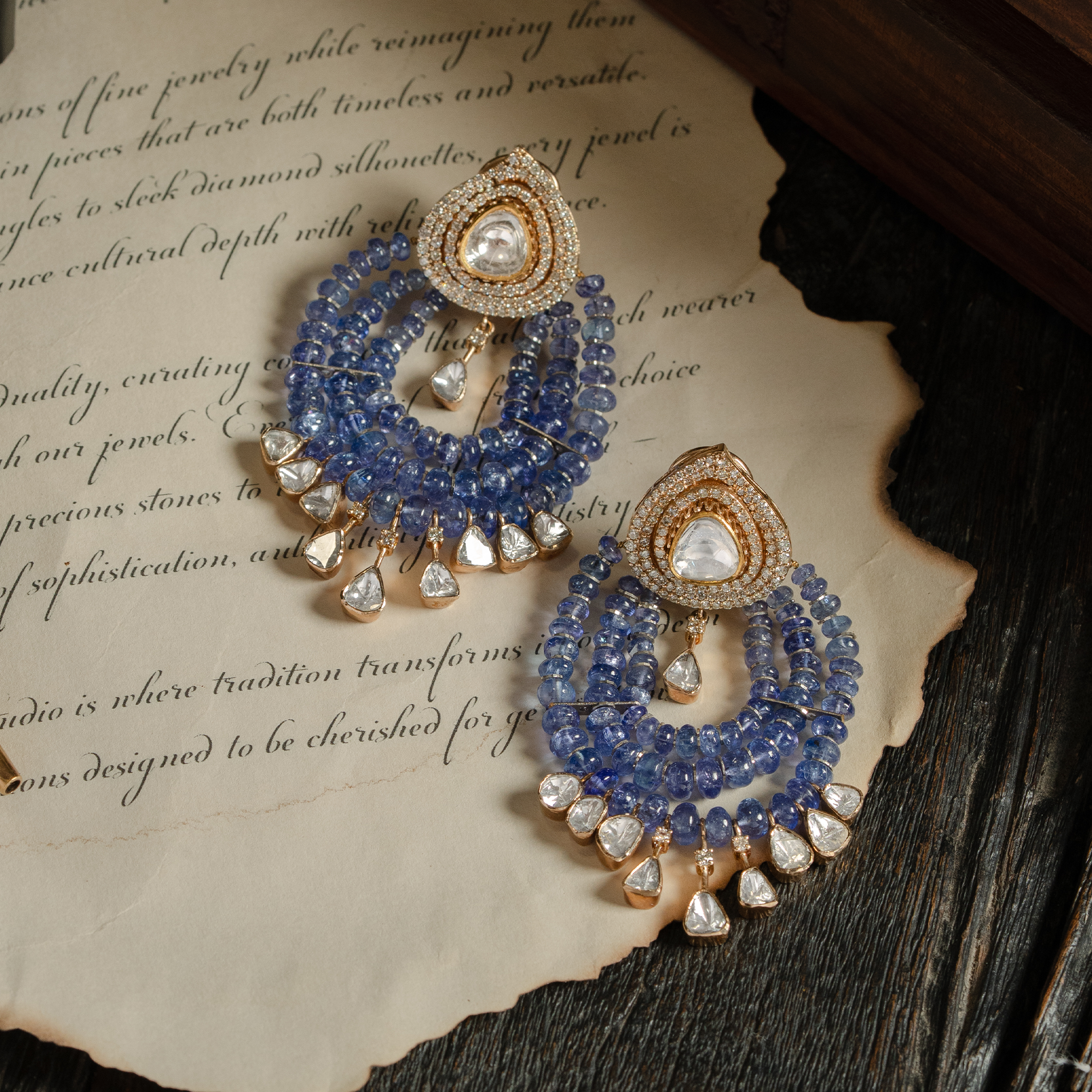A pair of ethereal blue tanzanite chandelier earrings featuring pear-shaped polki diamond studs and cascading multi-strand tanzanite bead swags finished with delicate diamond charms in india