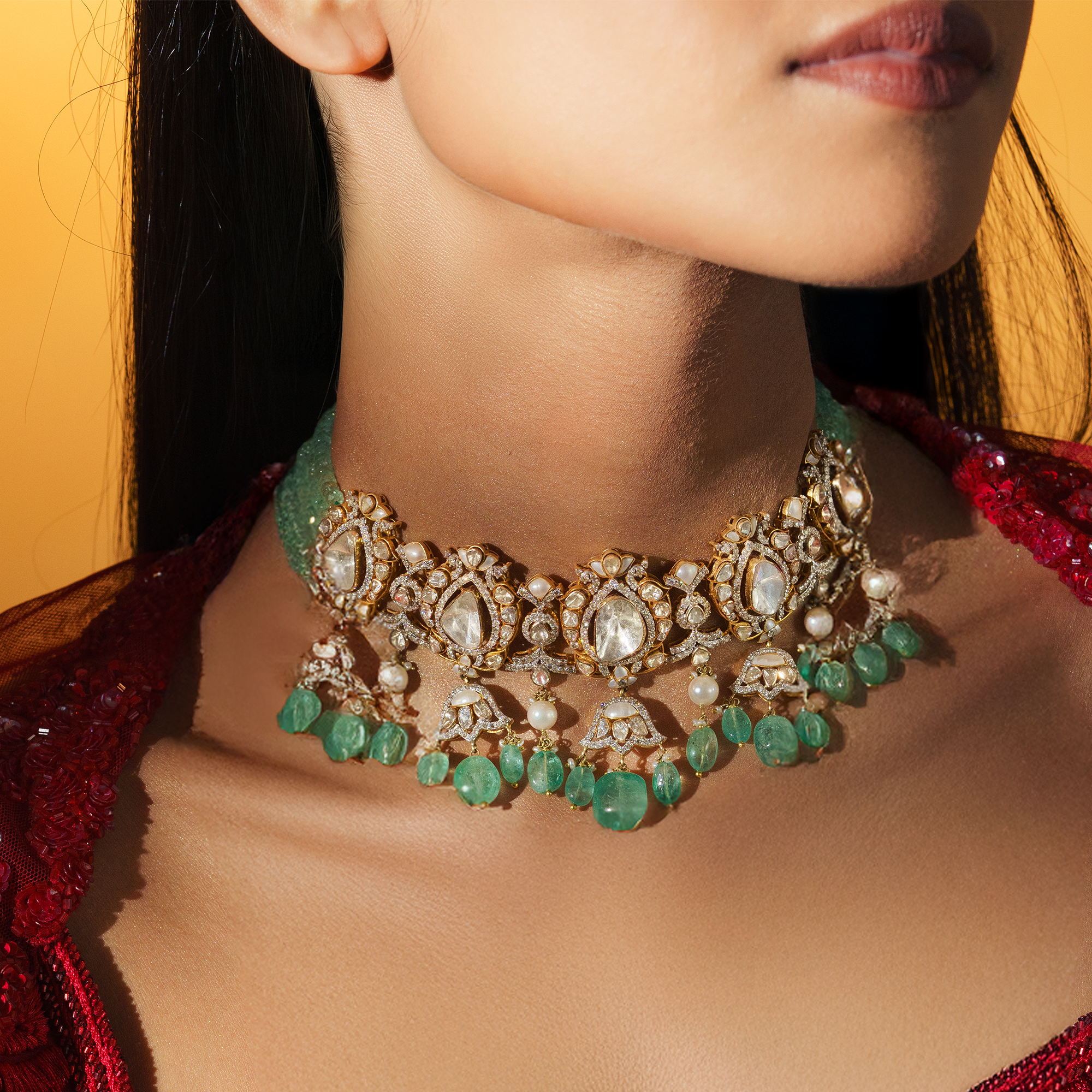 A model wearing a magnificent gold polki choker featuring a multiple strand of mint-green emerald beads and a central row of ornate uncut diamond floral motifs, finished with a lush fringe of pear-shaped emerald drops and seed pearls in india