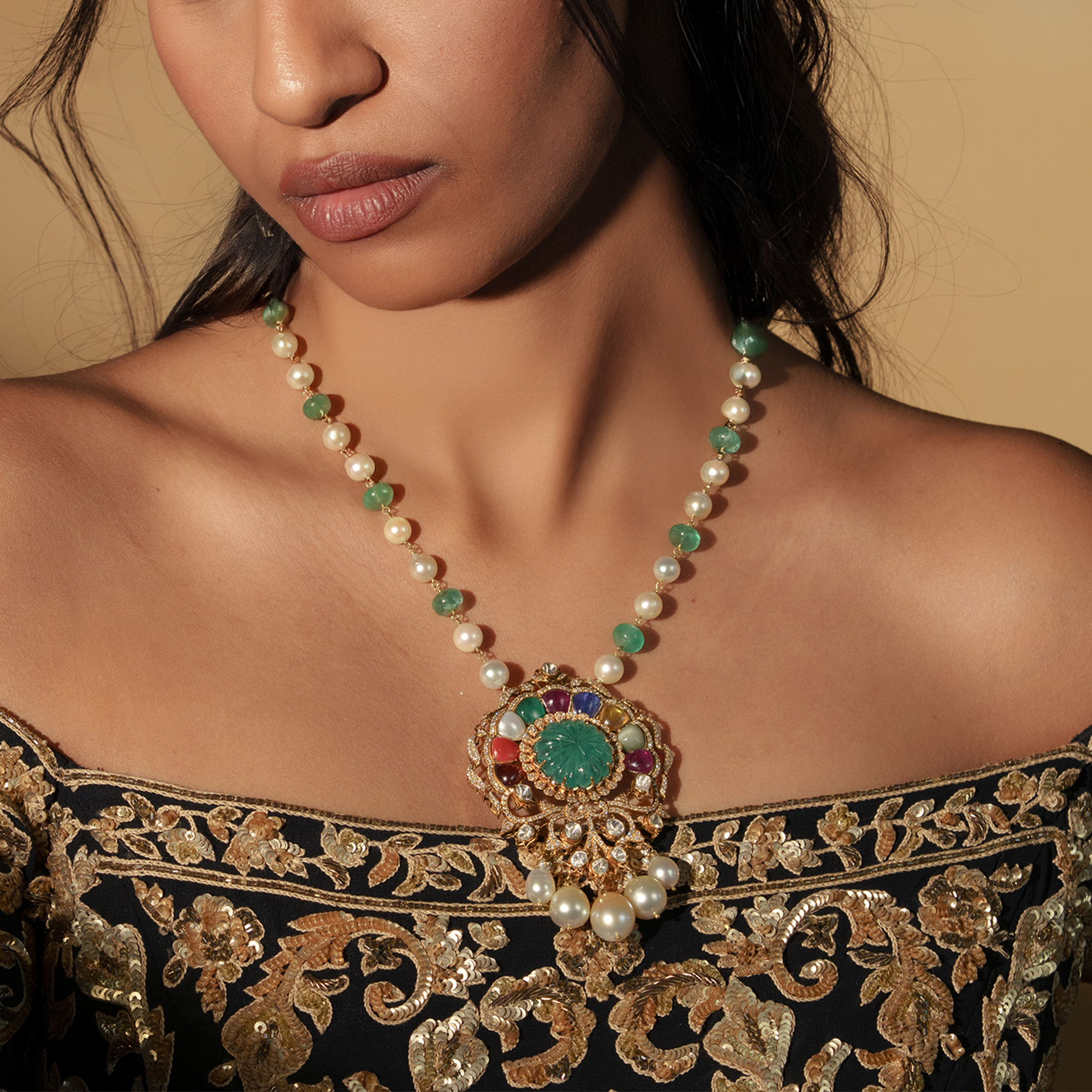 A model wearing a single strand of alternating pearl and emerald beads with a large, ornate pendant featuring a carved emerald center and multicolor Navratna gemstone accents in india