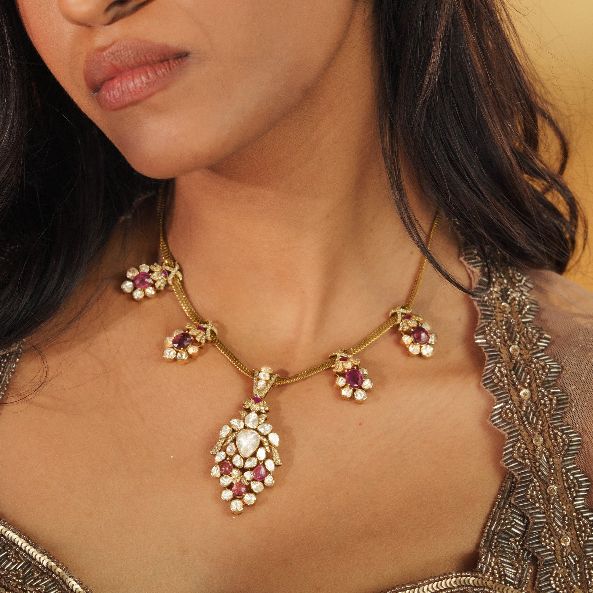 A model wearing a delicate gold chain necklace featuring four pink tourmaline and polki diamond floral charms and a large, coordinating pear-shaped drop polki pendant in india