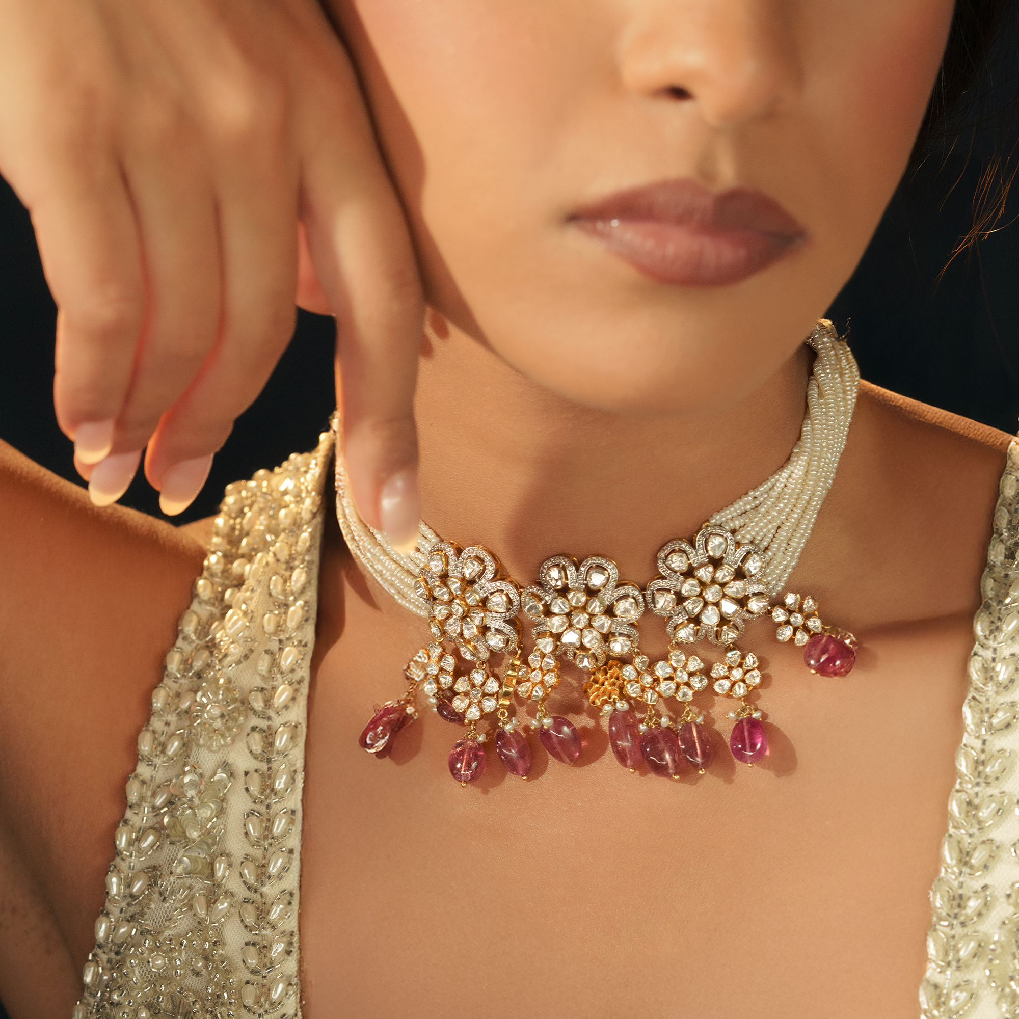A model wearing a delicate multi-strand seed japanese freshwater pearl choker featuring floral-motif polki diamond pendants and hanging ruby drops in india