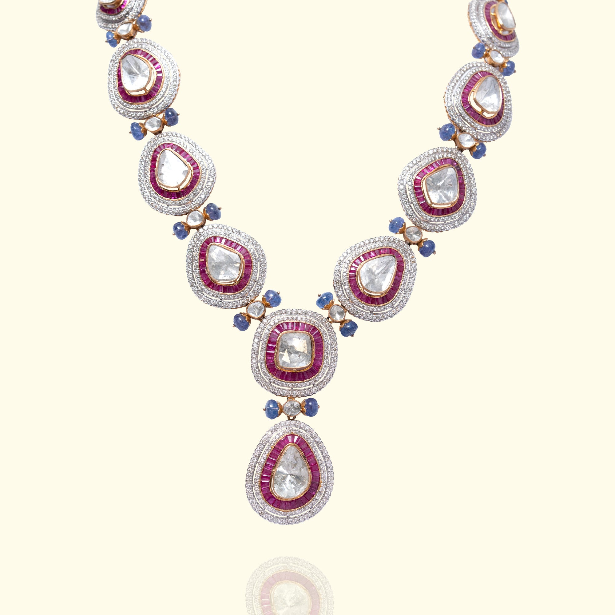 A majestic necklace featuring pear-shaped polki diamond links encased in ruby baguettes and shimmering pavé halos, accented by small blue sapphire beads.