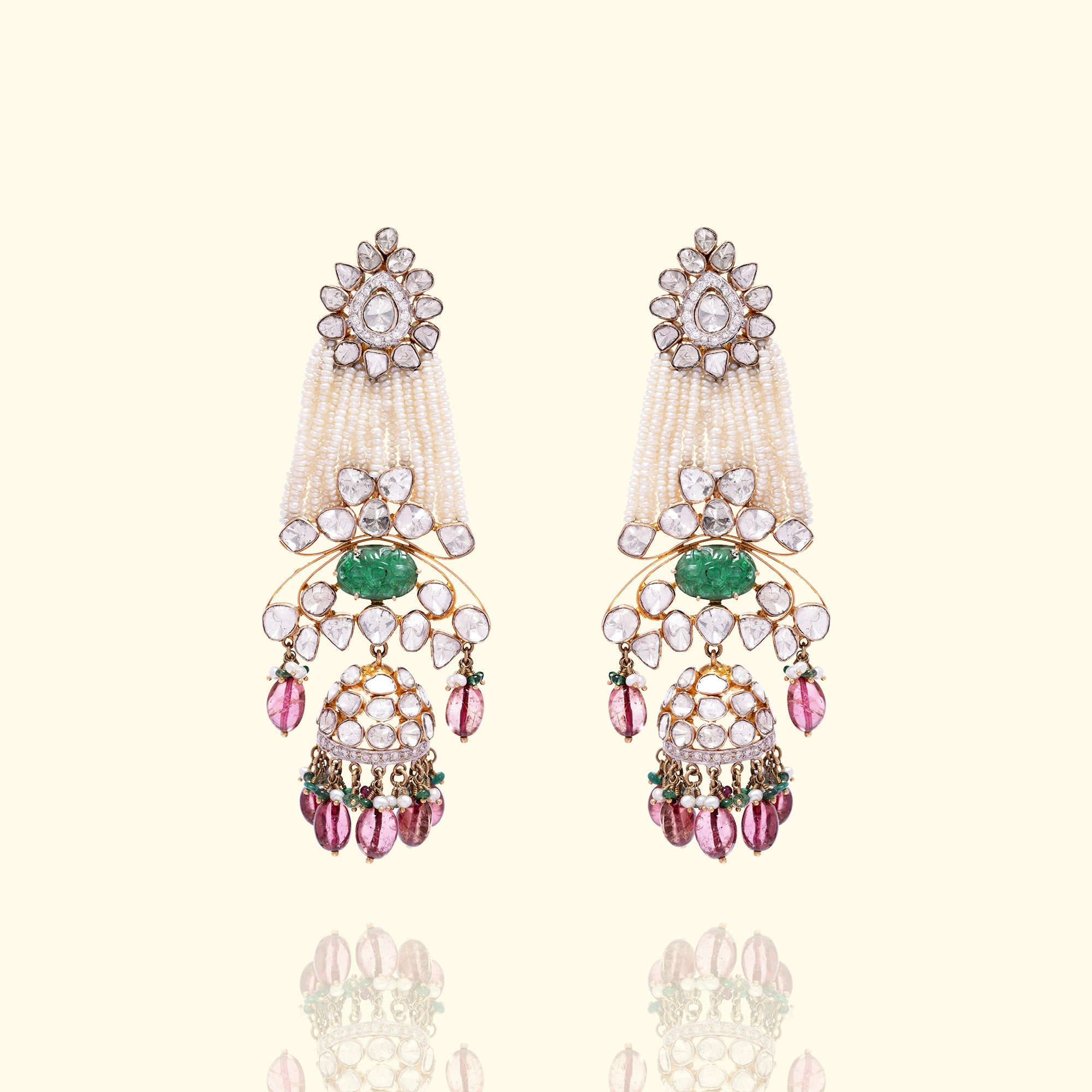 A pair of elaborate gold polki jhumka earrings featuring floral uncut diamond studs, multi-strand pearl tassels, and carved emerald accents with pink gemstone droplets.