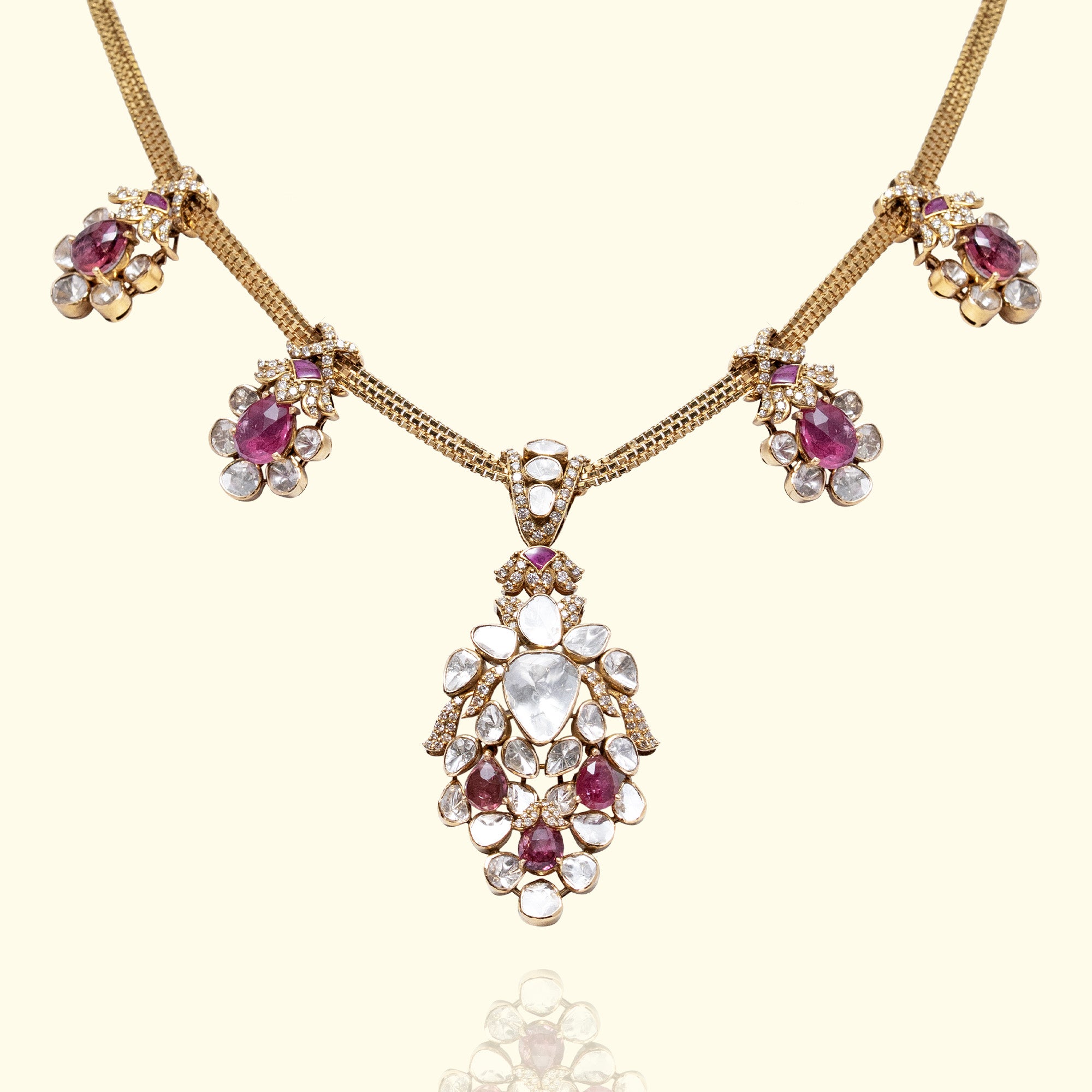 Gold Polki diamond statement necklace featuring a large floral pendant with pink tourmaline accents and matching pink tourmaline-set charms on a gold chain.