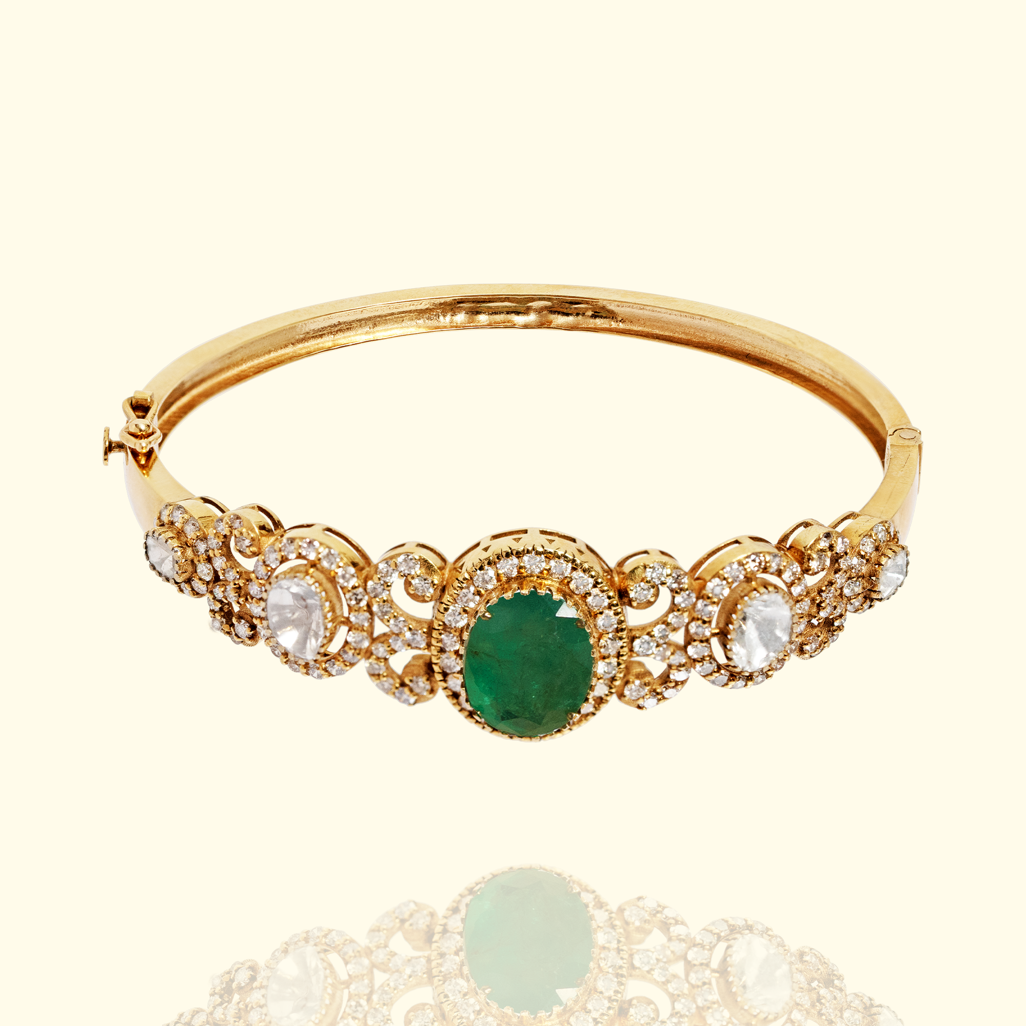A sophisticated gold bangle featuring a central oval-cut emerald centerpiece surrounded by ornate diamond scrollwork and oval-shaped polki diamond accents.