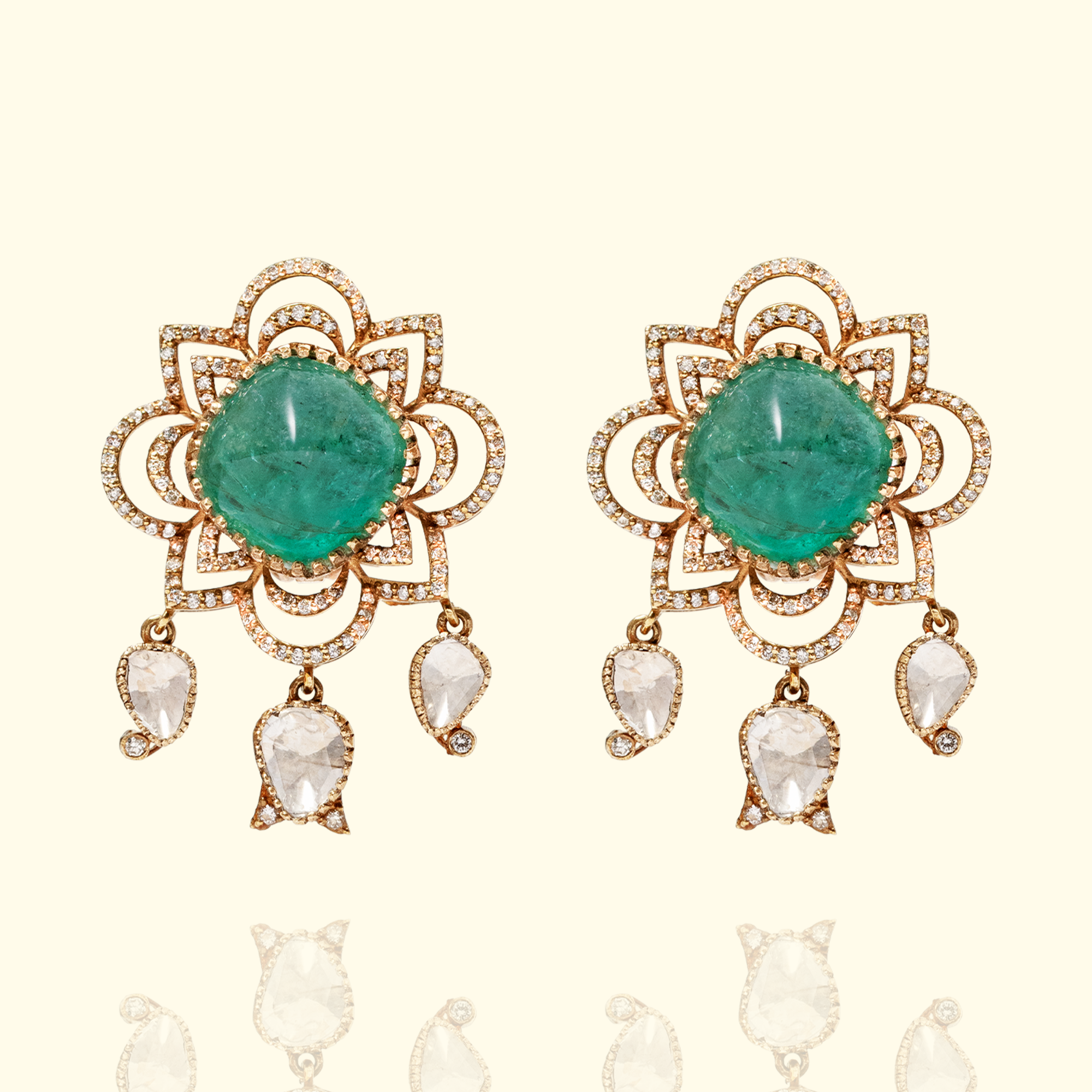 A pair of ornate floral stud earrings featuring large, cushion-cut emerald cabochons set within a diamond-encrusted lotus motif with hanging pear-cut polki diamond charms.
