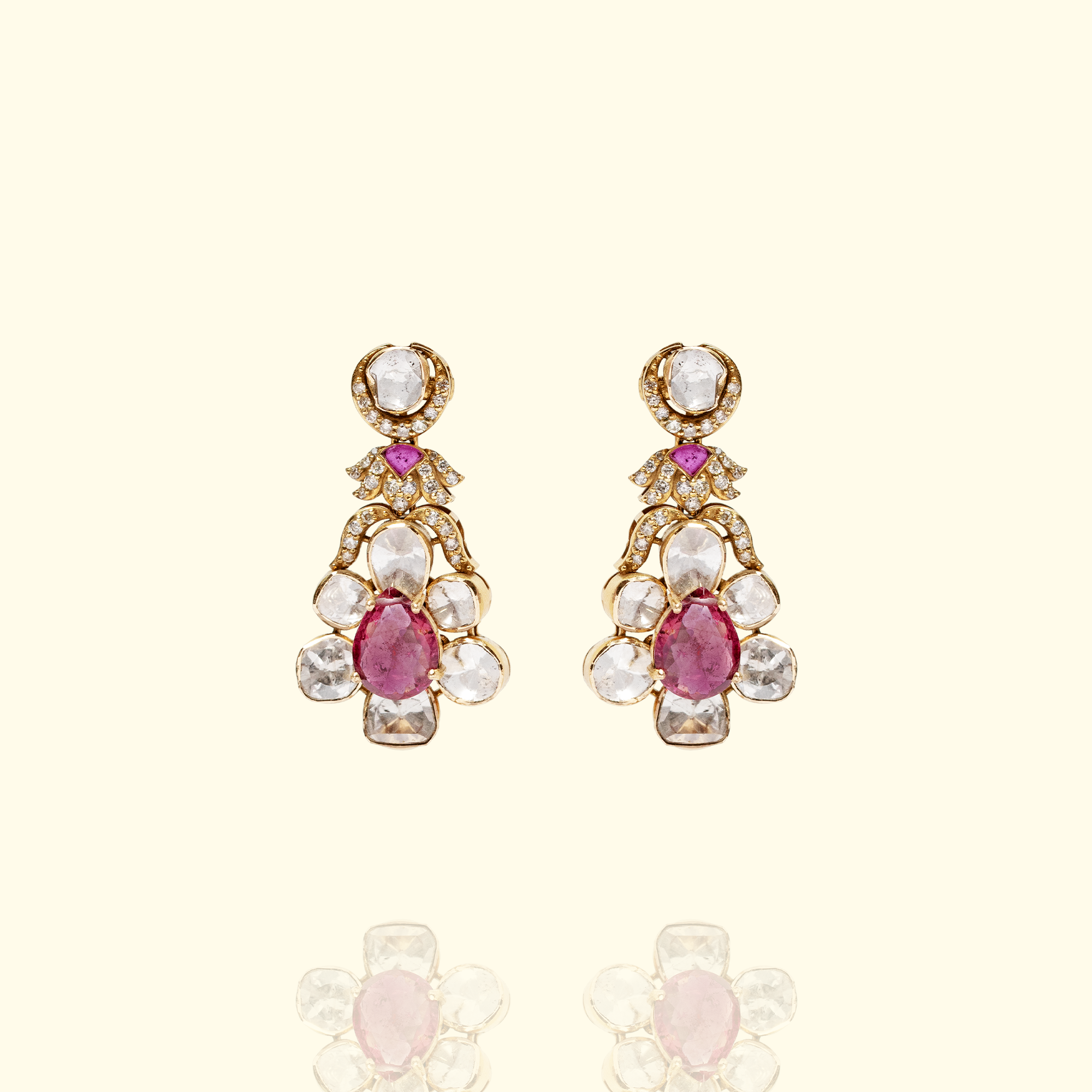 A pair of ornate gold drop earrings featuring a central pear-cut ruby surrounded by a polki diamond flower motif and diamond pavé accents.