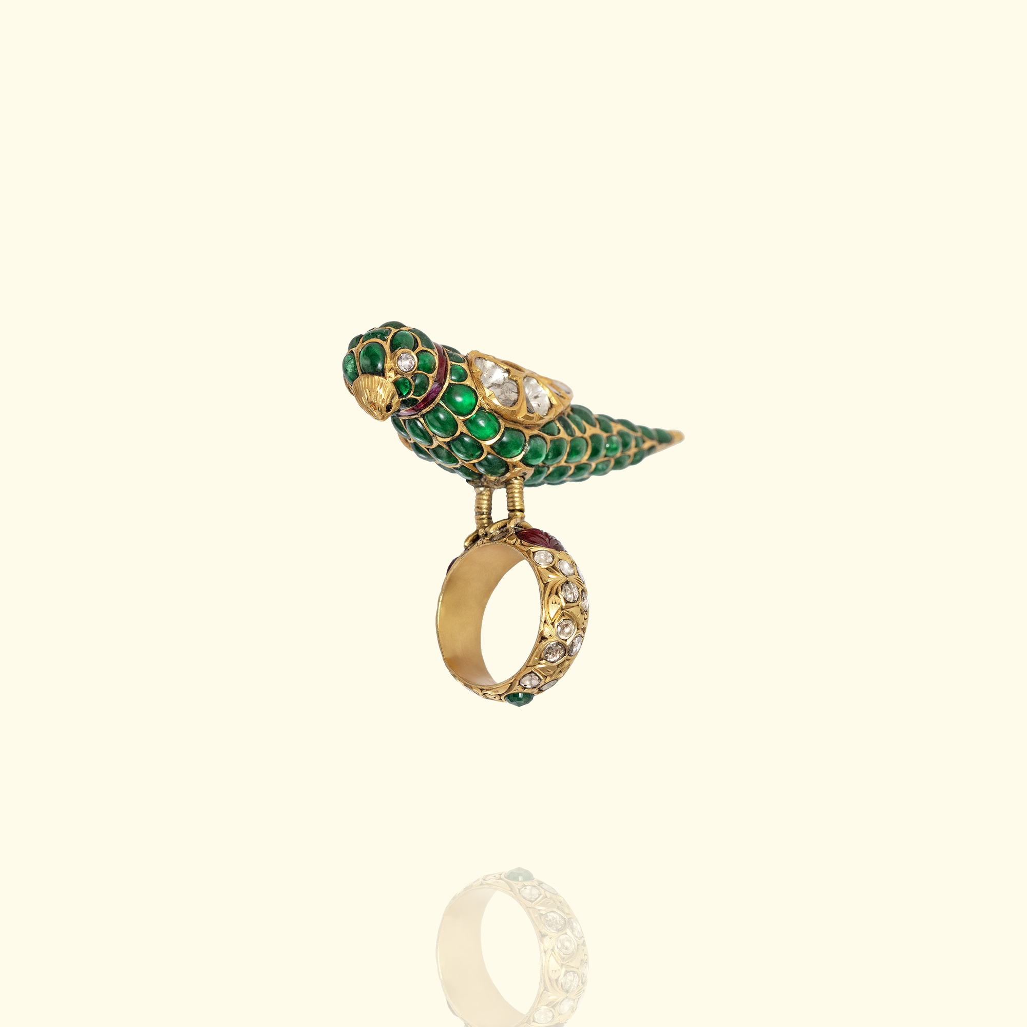 Traditional gold parrot statement ring featuring green cabochon gemstone inlay, ruby accents, and a wide band set with uncut diamonds and floral engravings.