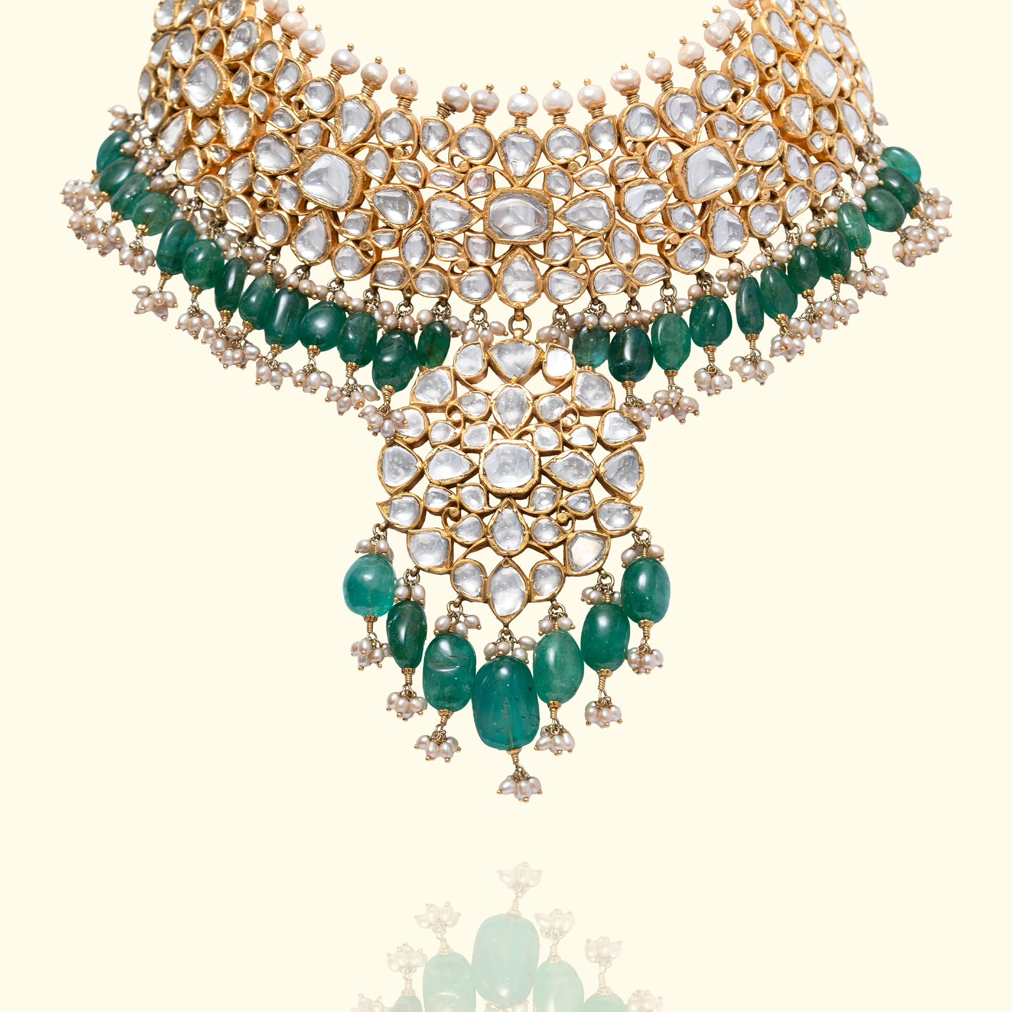 A high-neck gold polki choker featuring a dense mosaic of pear and heart-shaped uncut diamonds, accented with a double fringe of vibrant emerald beads and a central, oversized polki diamond pendant.