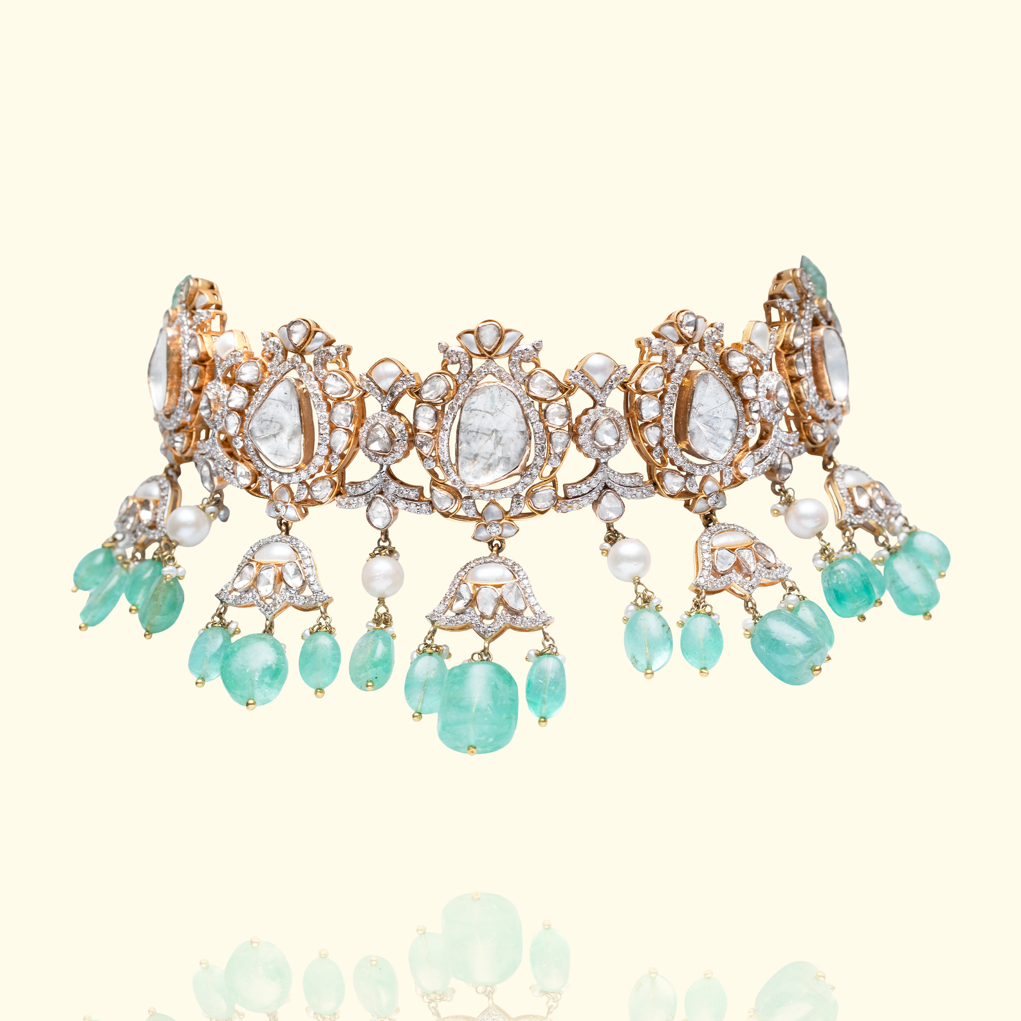 A high-jewelry gold choker featuring ornate lotus-motif polki stations accented with small pearls and large, vibrant emerald droplets.