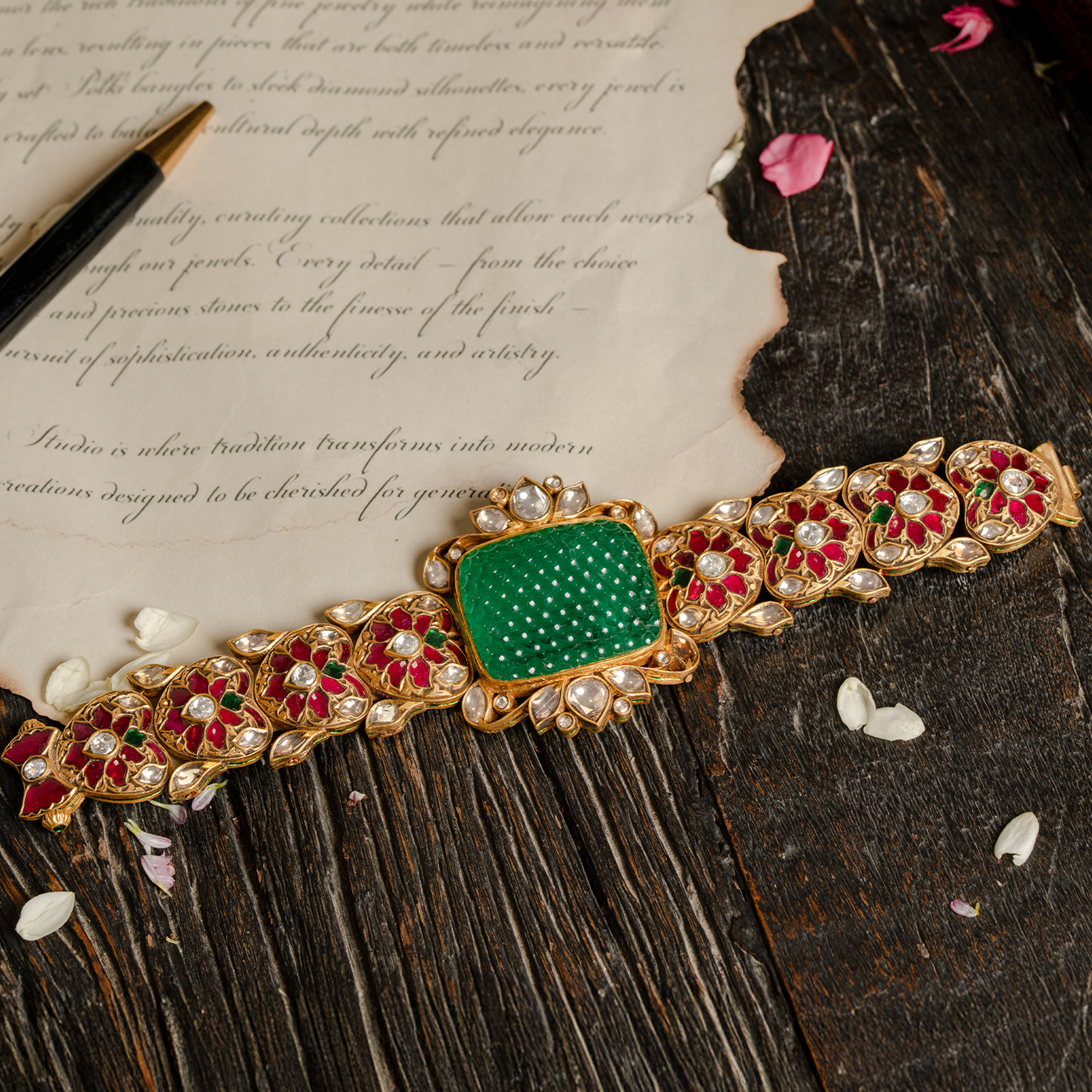 An ornate gold link bracelet featuring a large, textured square-cut carved emerald flanked by intricate ruby and polki diamond floral-motif links.