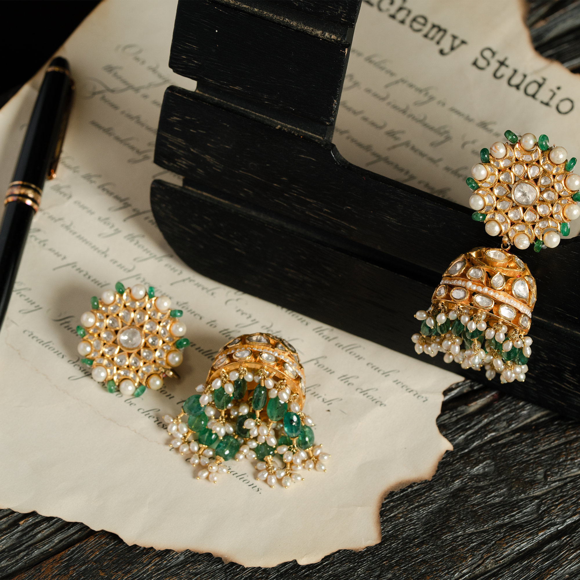 A pair of ornate gold chandelier earrings featuring circular polki diamond studs rimmed with pearls and emeralds, finished with bell-shaped jhumkas and cascading emerald bead tassels.