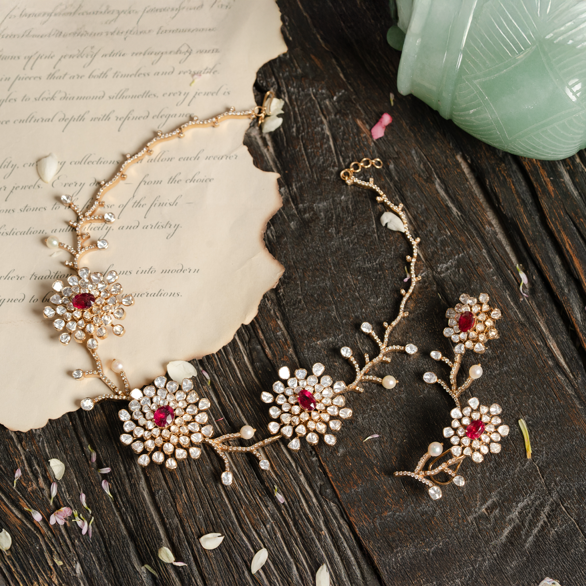 An exquisite gold polki ruby jewelry set featuring a necklace designed as a delicate twining vine with diamond-encrusted stems, blooming with floral motifs centered by oval rubies and uncut diamond petals, accompanied by matching floral drop earrings.