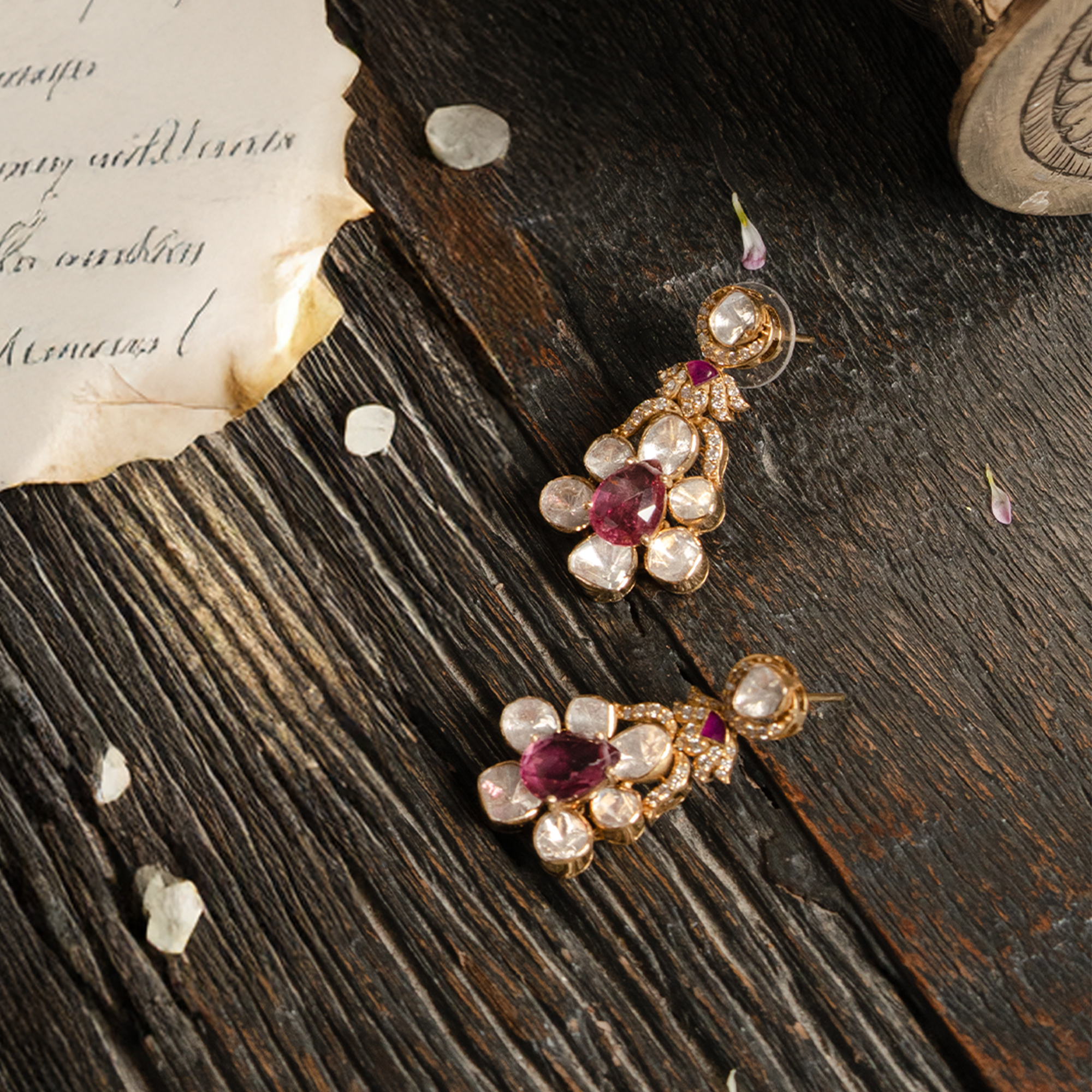 A pair of ornate gold drop earrings featuring a central pear-cut ruby surrounded by a polki diamond flower motif and diamond pavé accents.