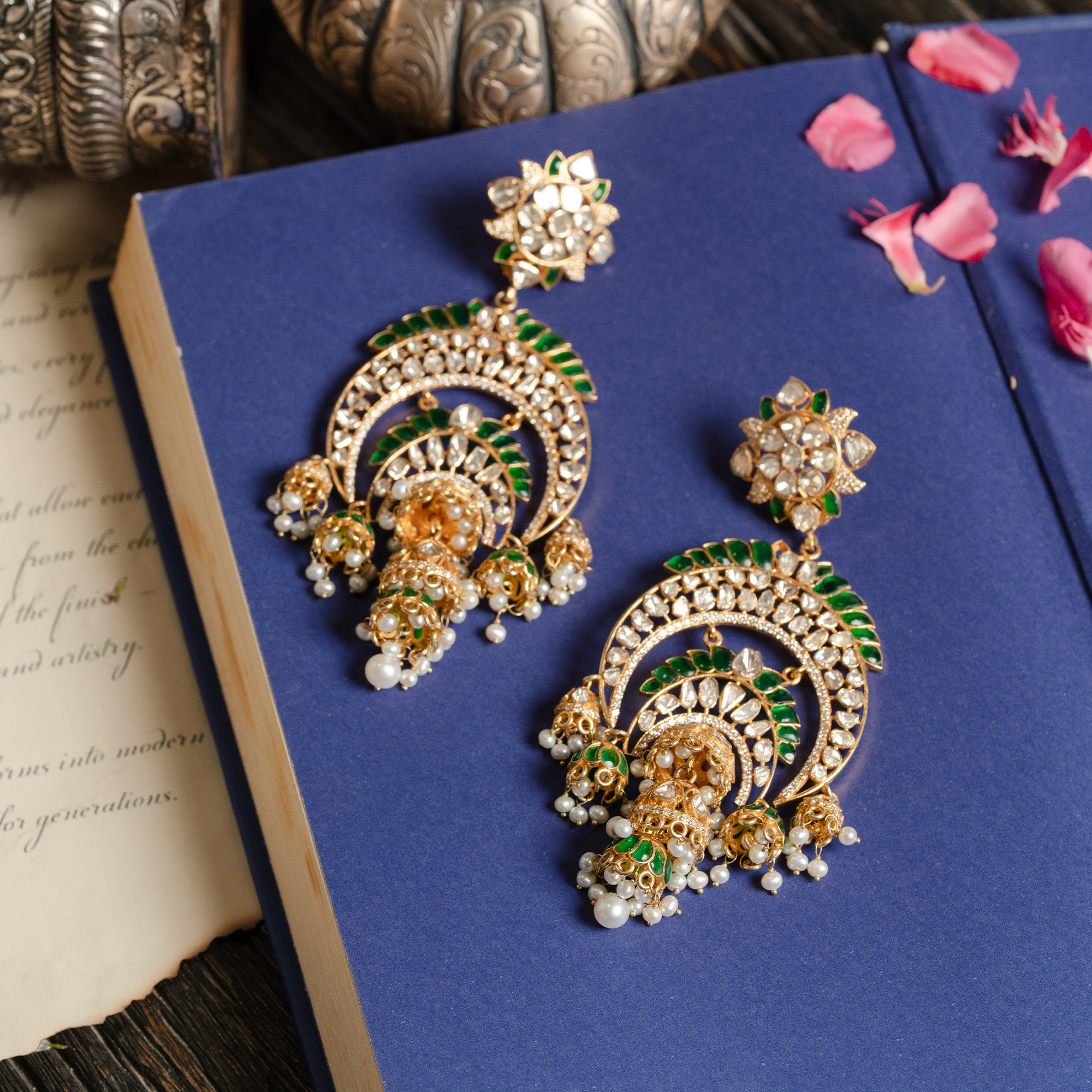 A pair of elaborate gold chandbali earrings featuring floral polki studs, intricate crescent tiers lined with vibrant green enamel, and finished with dangling japanese freshwater pearls and bell-shaped jhumka charms.