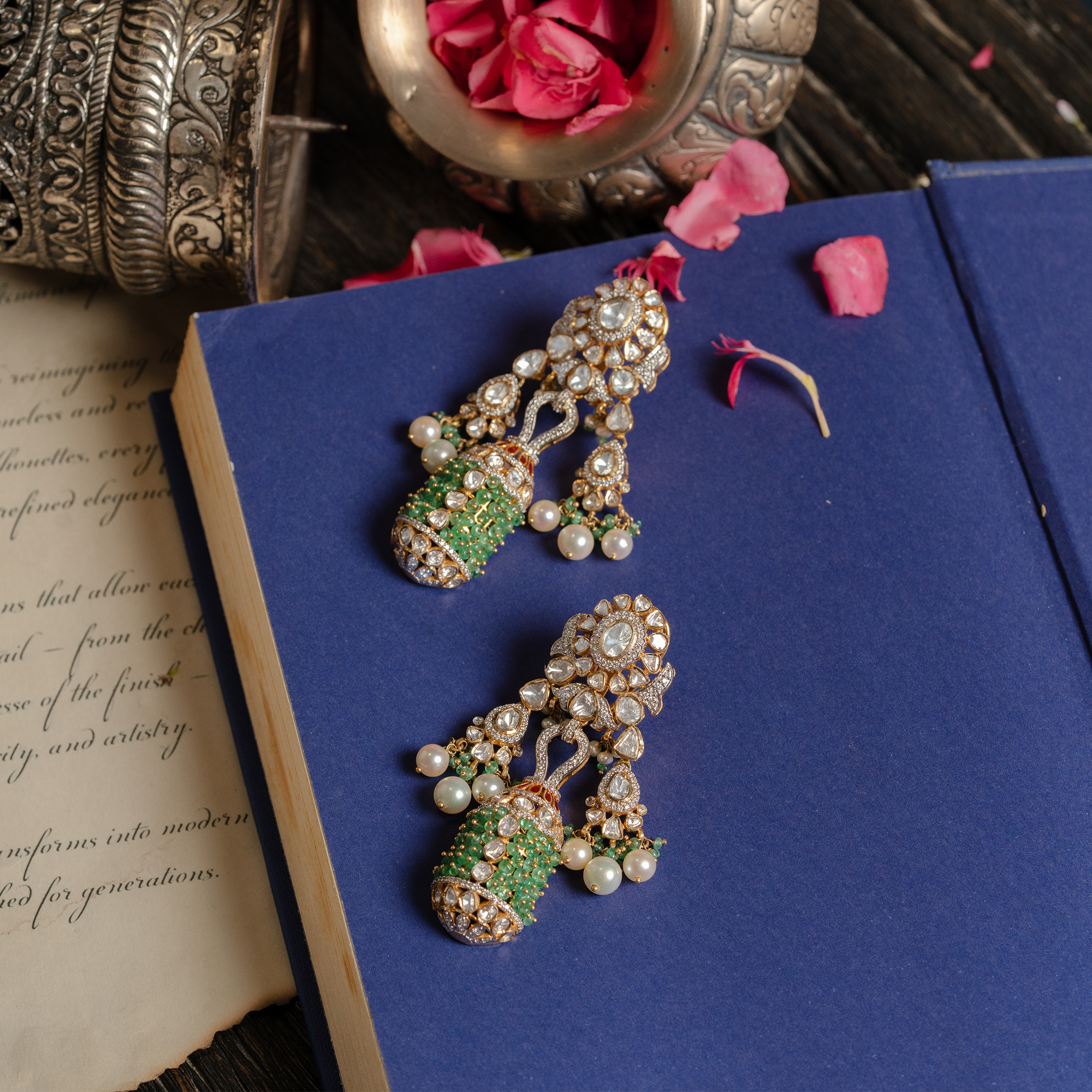 A pair of ornate gold polki earrings featuring a floral uncut diamond stud that supports a unique cylindrical tassel encrusted with vibrant emerald beads, accented by small japanese freshwater pearl drops and delicate brilliant cut diamond-set scrollwork.