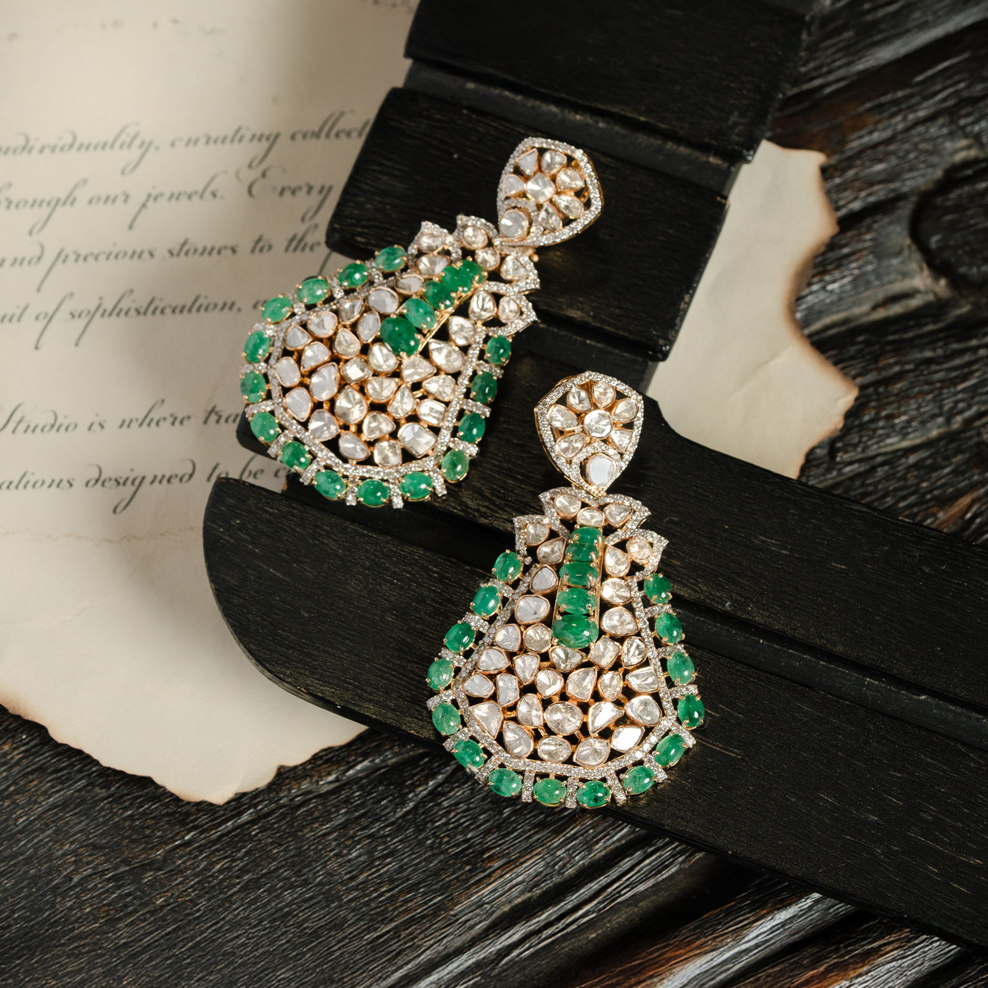 A pair of large, pear-shaped drop earrings featuring a mosaic of polki diamonds framed by a vibrant border of emerald and shimmering pavé round diamonds.