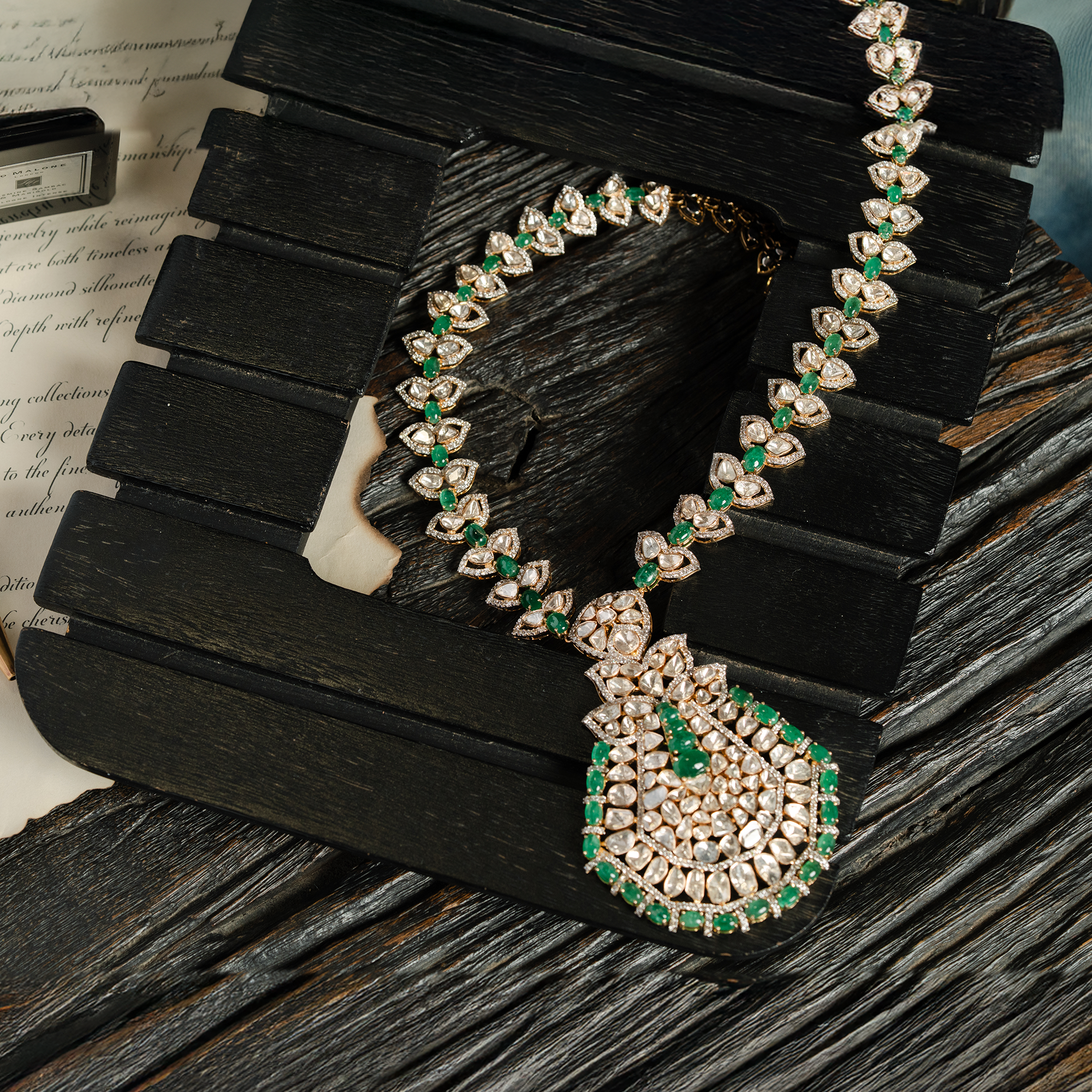 A magnificent long necklace featuring a chain of leaf-motif polki diamond links accented with emerald beads, leading to an oversized, pear-shaped mosaic pendant of polki diamonds and vibrant emerald beads in india