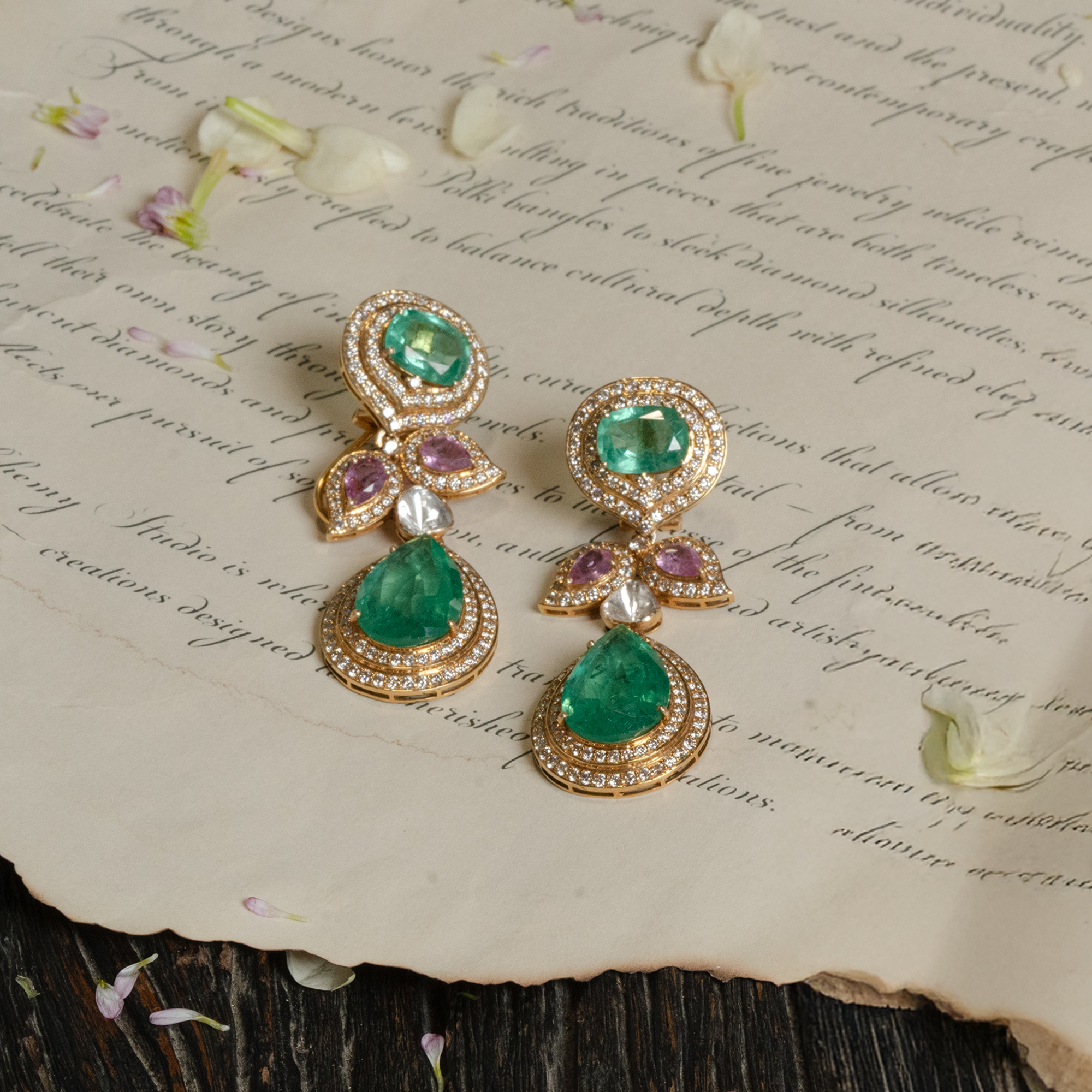 A regal triple-tier drop earrings featuring a round emerald stud, a leaf-motif center with pink sapphires, and a large pear-cut emerald drop, all encased in shimmering diamond halos.