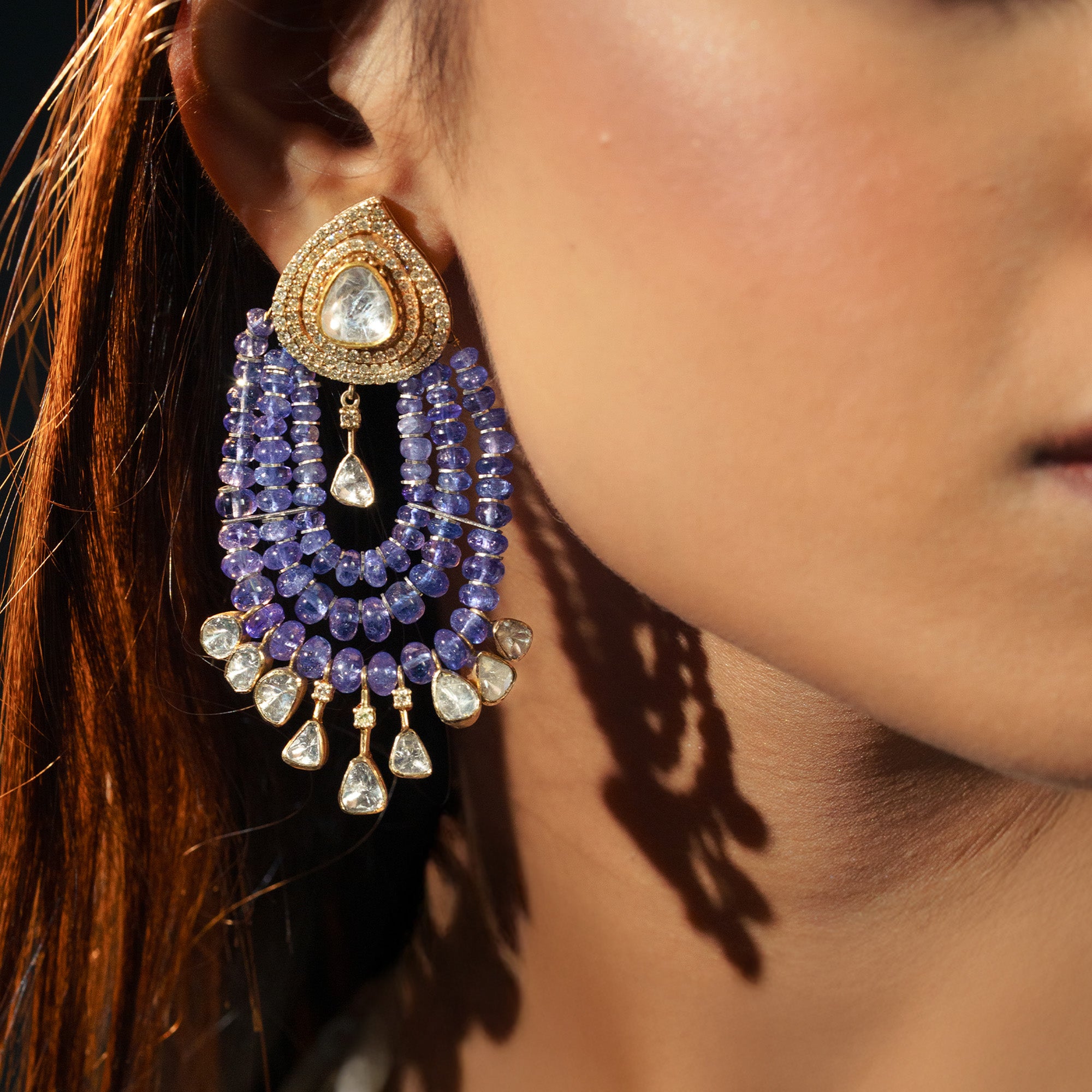 Side profile of a model wearing gold Polki and tanzanite tassel earrings featuring pear-shaped diamond studs and cascading blue tanzanite beads.