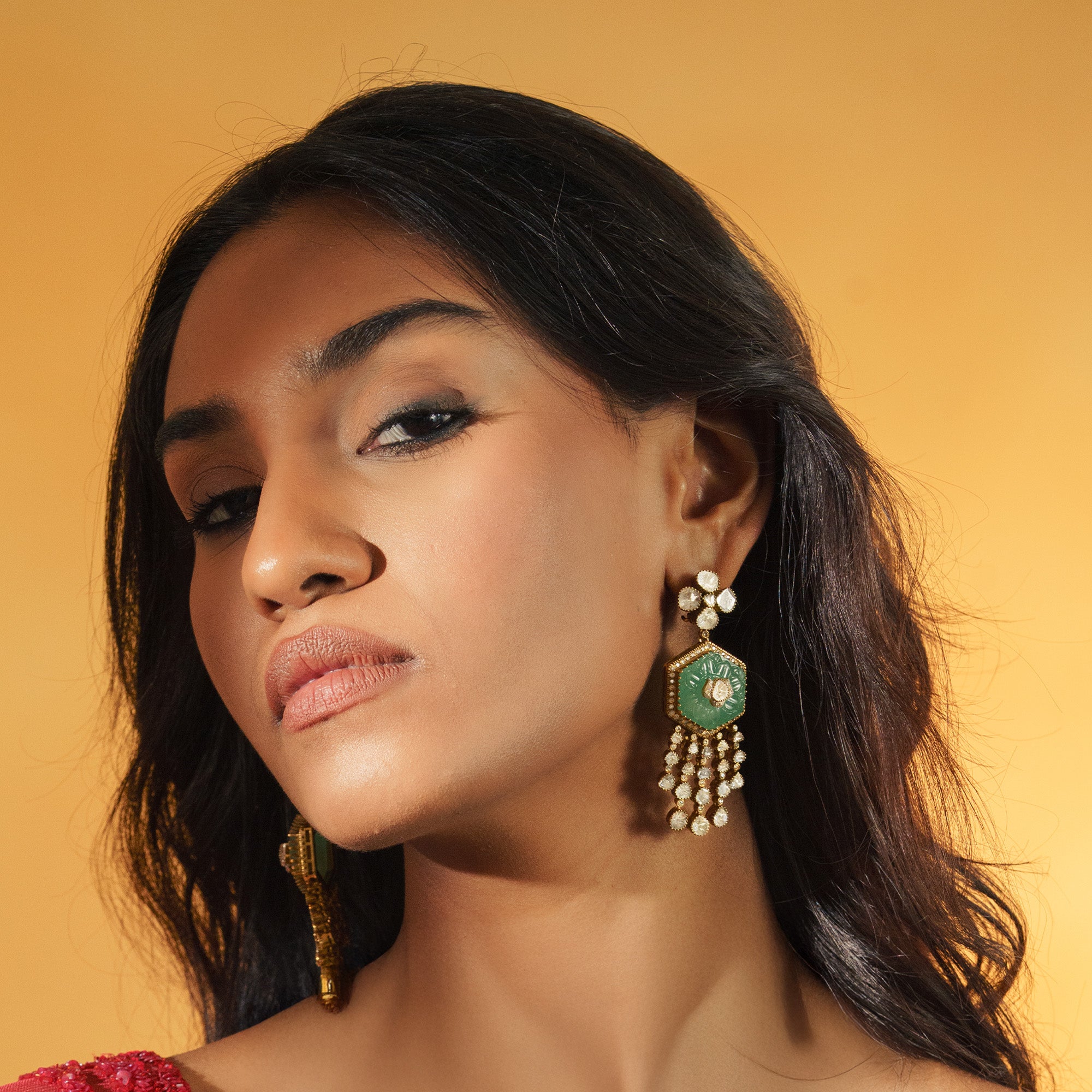 A model wearing a striking hexagonal carved emerald earring featuring a floral polki diamond stud and multiple cascading uncut diamond-encrusted tassels.