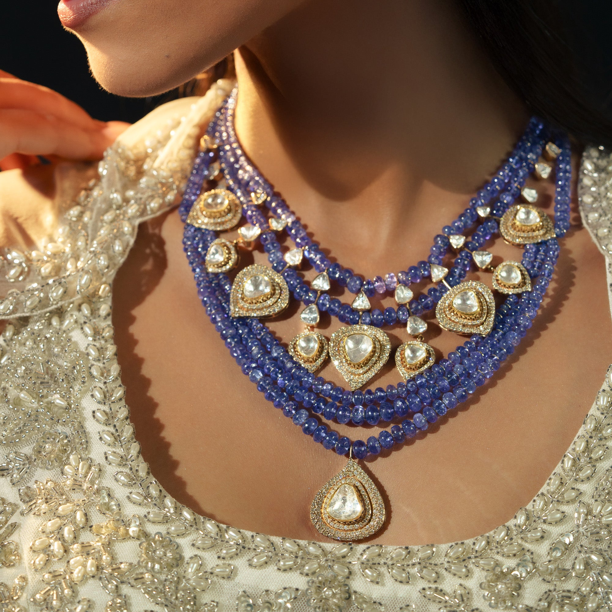 A model wearing a magnificent multi-strand tanzanite bead necklace featuring graduated rows of blue-violet beads and multiple pear-shaped polki diamond pendants set in shimmering halos.