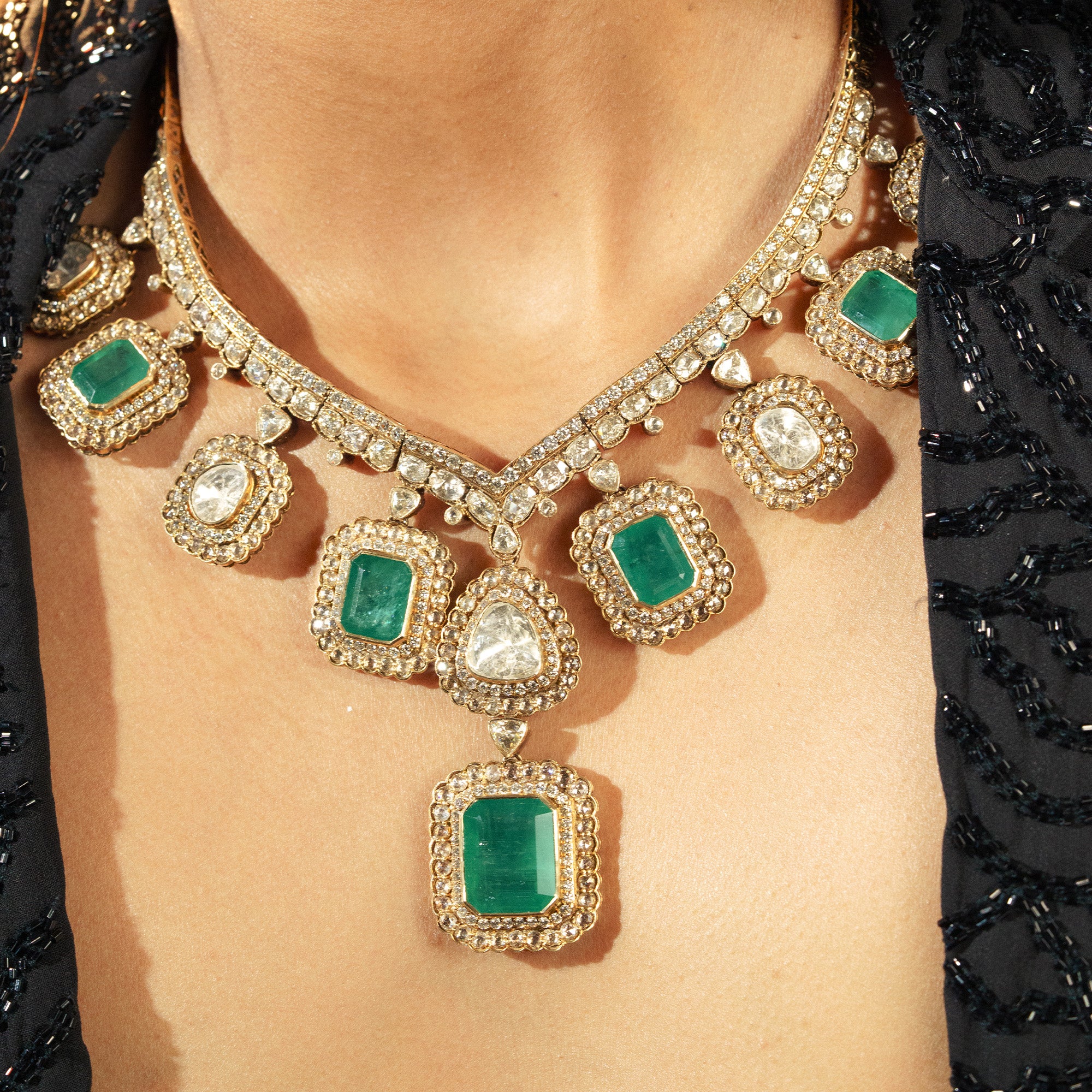 Close-up of a model wearing gold Polki earrings with a central green emerald cabochon surrounded by an intricate diamond lattice and dangling charms.