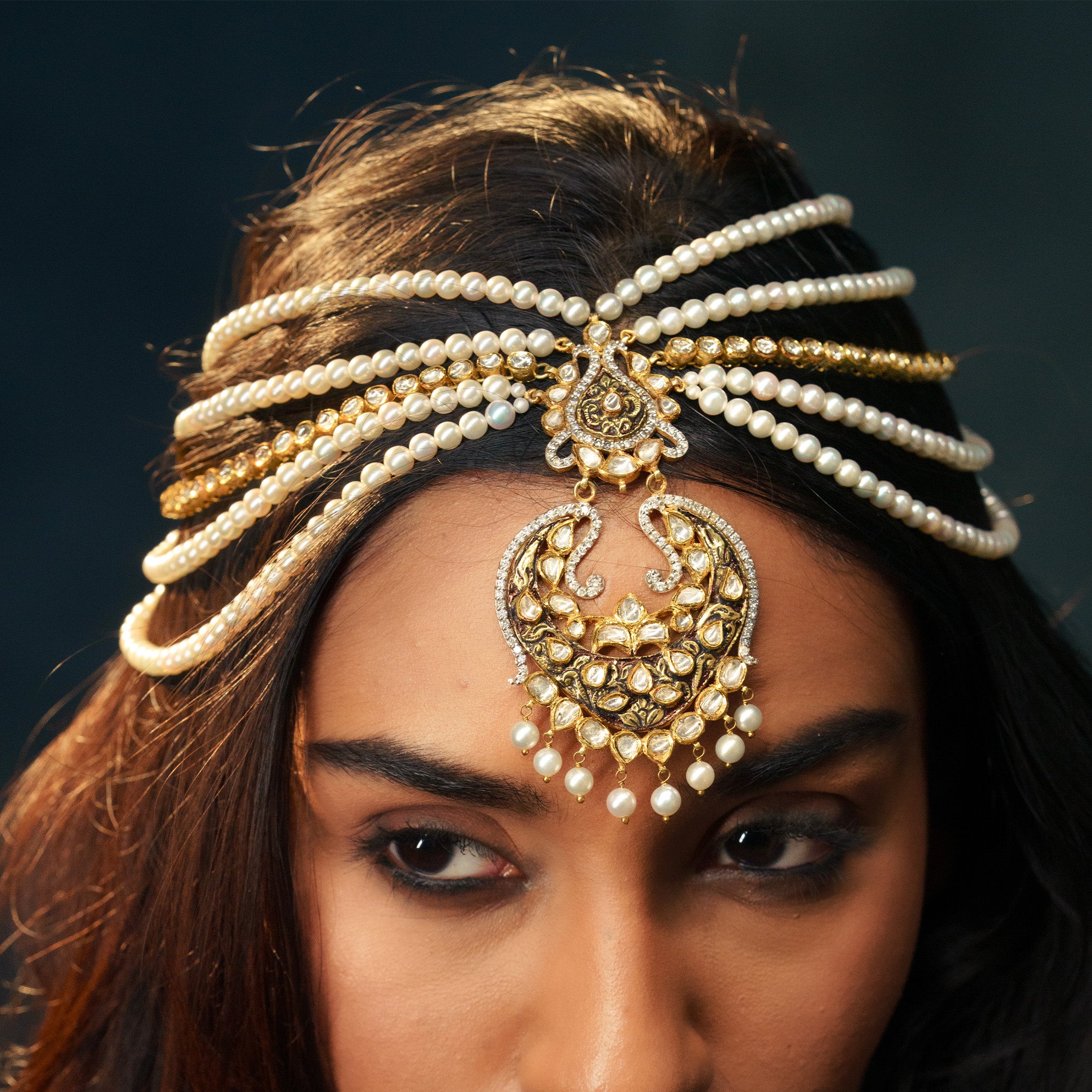 A model wearing a wide gold choker featuring geometric and floral polki diamond settings, topped with a row of small pearls and finished with a lush fringe of vibrant emerald bead drops.
A multi-strand japanese freshater pearl necklace featuring an ornate gold pendant with intricate polki diamond scrollwork in a traditional crescent (chandbali) silhouette, accented with hanging pearl drops.