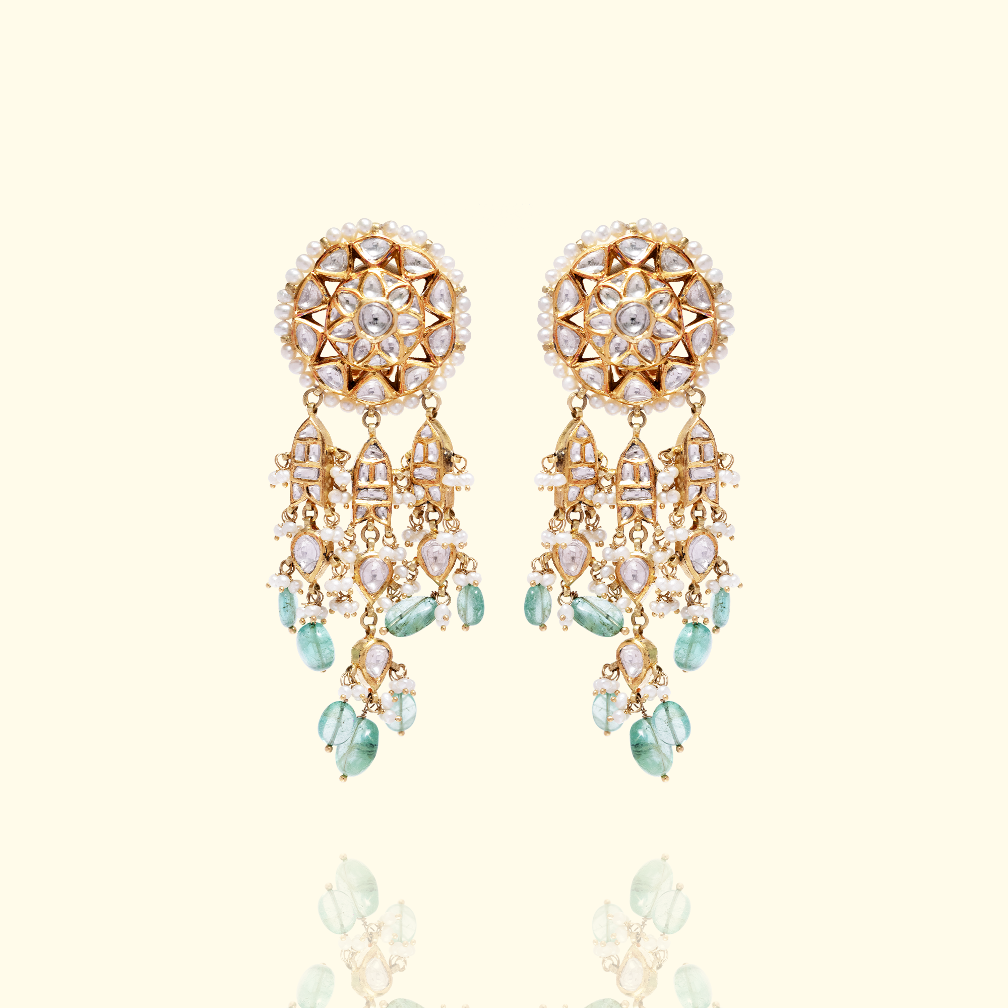 Pair of gold Polki chandelier earrings featuring floral-motif studs edged with pearls and dangling pear-shaped polki diamond and emerald accents.