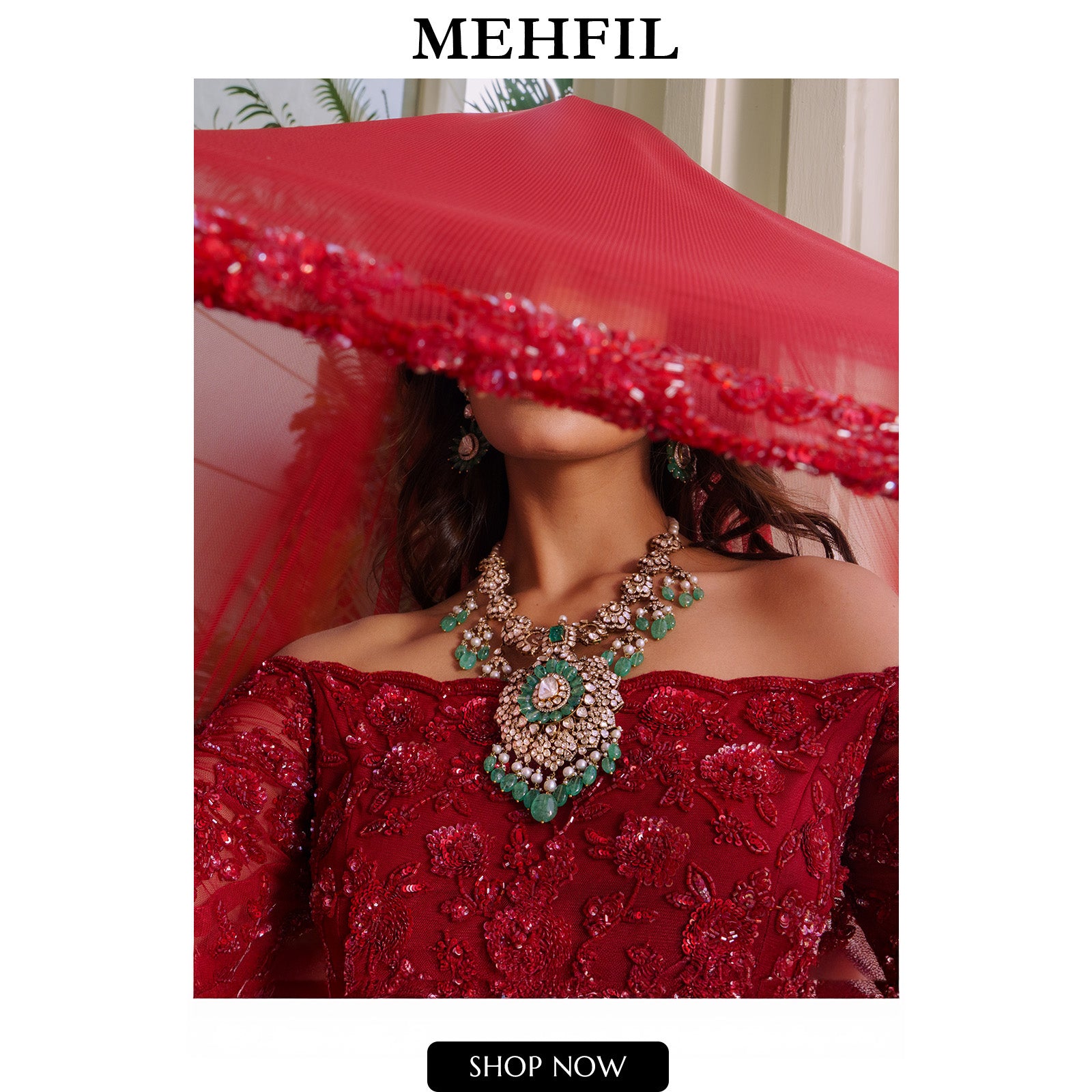 A model wearing a sheer red veil and a full suite of traditional gold jewelry, including an ornate maang tikka with pink stones and emerald drops, a statement emerald and polki cocktail ring, and stacked polki diamond bangles.