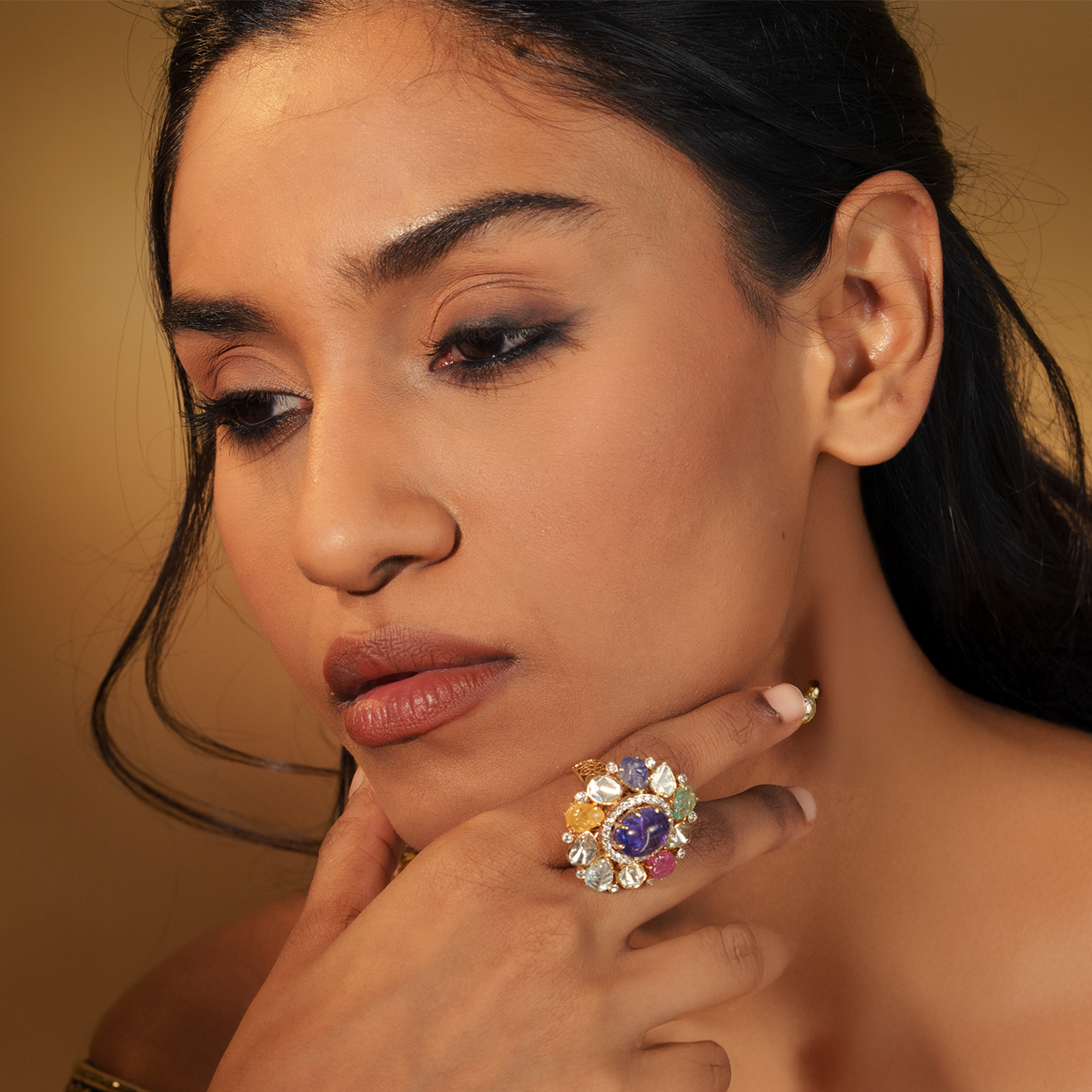A model wearing a vibrant cocktail ring featuring a central purple sapphire surrounded by a halo of multicolored navratan gemstones and polki diamonds.