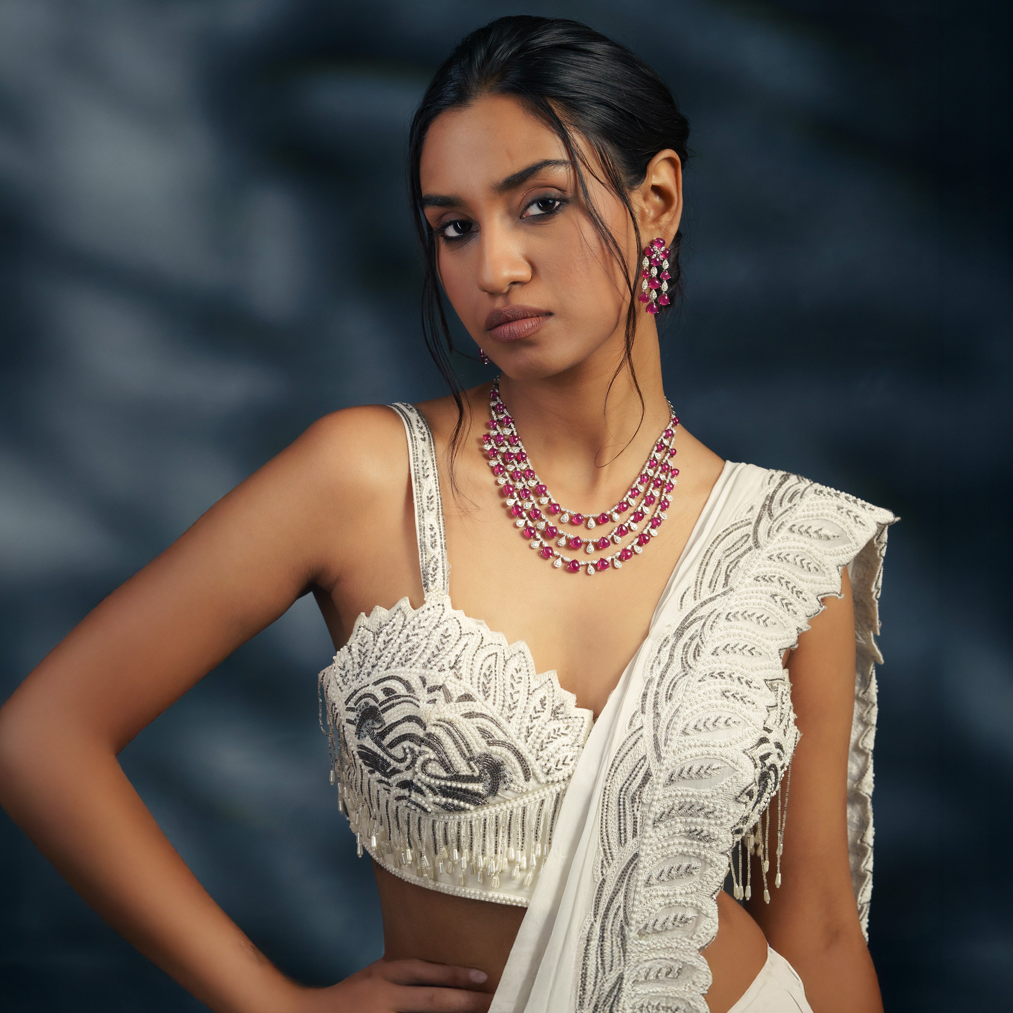 Elegant three-string ruby and diamond necklace set in white gold, paired with matching ruby floral drop earrings and a white designer saree for a modern bridal look.