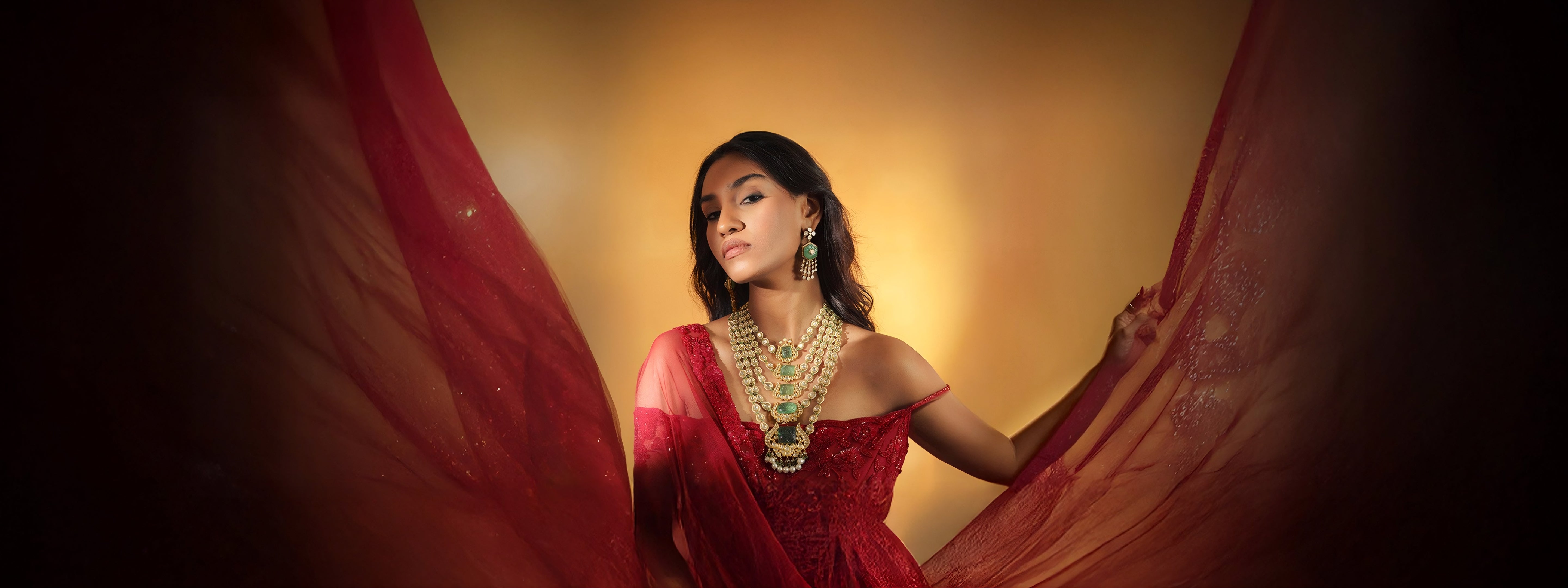A model wearing a luxurious Indian bridal jewelry set featuring a heavy gold uncut polki diamond necklace with square-cut carved emerald, matching chandelier polki emerald earrings, and a large polki diamond statement ring.
