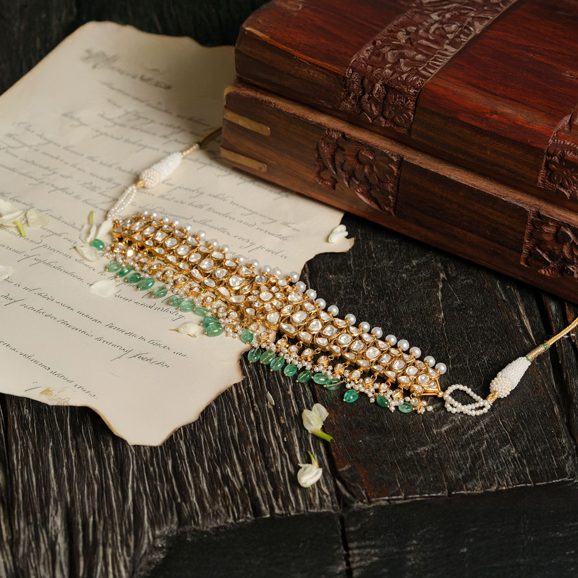 A magnificent high-glamour look featuring a pearl-strung polki choker layered with a wide, tiered gold bib necklace encrusted with teardrop polki diamonds and a lush emerald fringe.