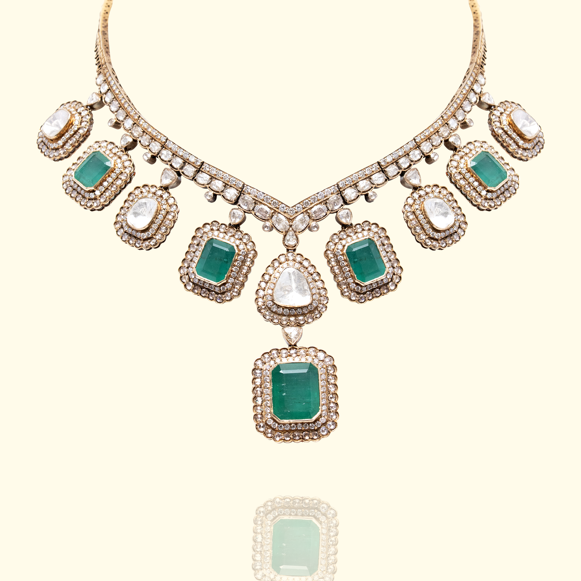 A majestic gold collar necklace featuring alternating square-cut emeralds and polki diamonds, each framed by a shimmering diamond halo in india
