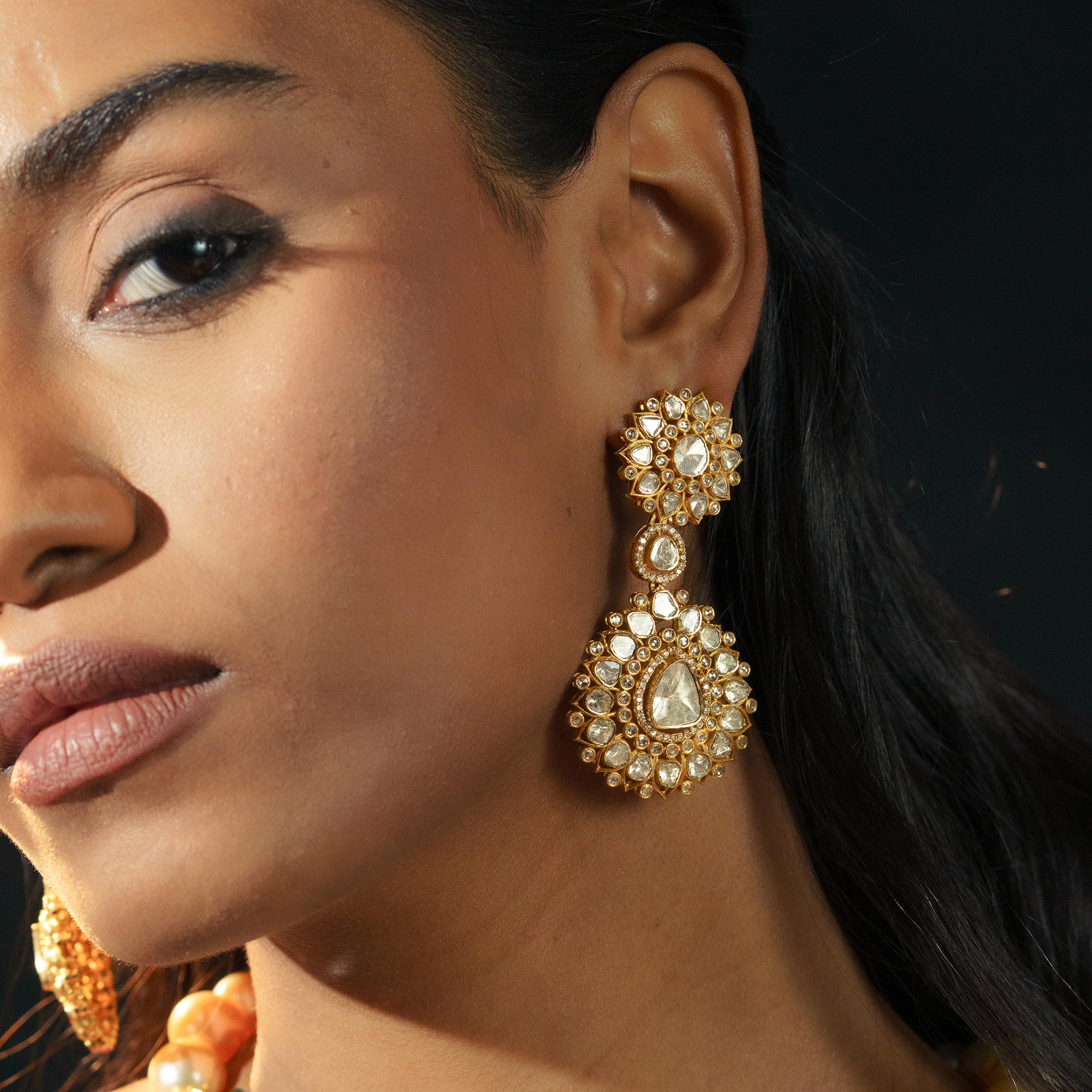 A model wearing elegant gold double-drop earrings featuring two tiers of sunflower-motif polki diamonds with delicate pavé borders in india