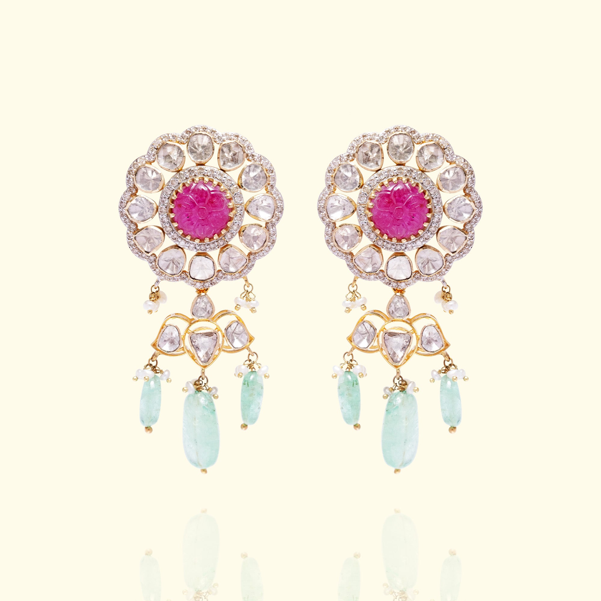 A pair of ornate floral-motif gold polki earrings featuring a central carved ruby cabochon surrounded by uncut diamonds and finished with cascading emerald droplets.