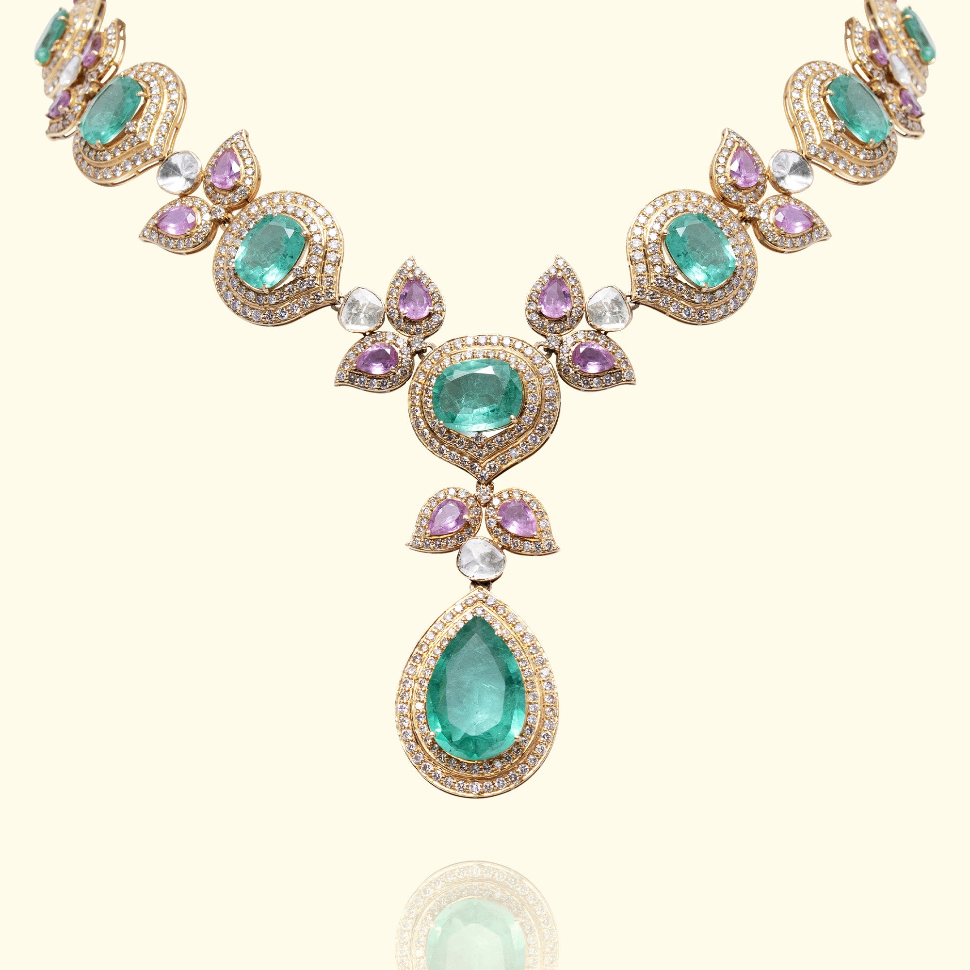 A luxury gold statement polki emerald tourmaline necklace featuring a graduated series of vibrant oval emerald framed by diamond-pavé halos and accented with delicate amethyst petals and pear-shaped polki diamonds.