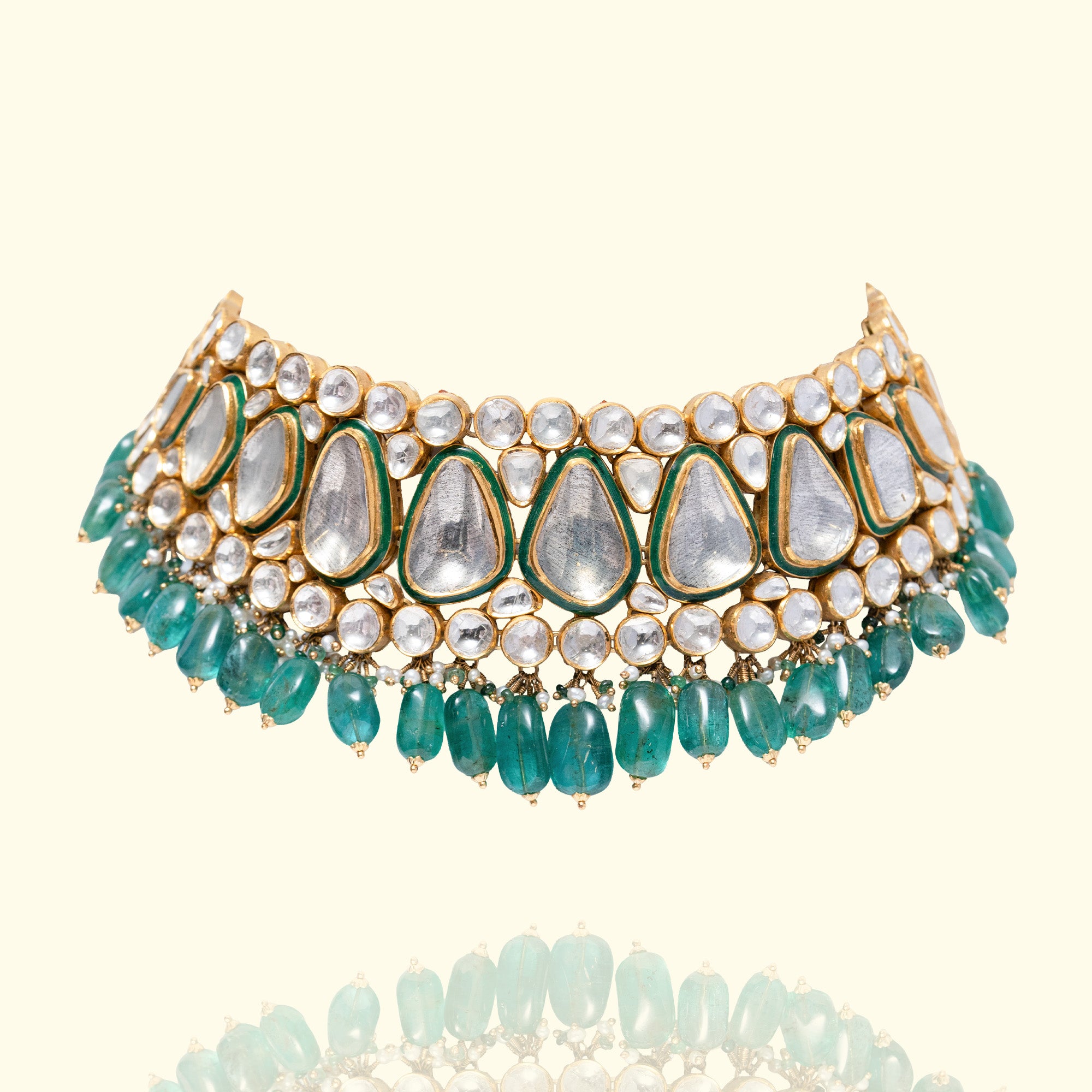 Studio shot of a broad gold Polki diamond choker featuring large pear-shaped centers with green enamel borders and a dense emerald bead fringe.