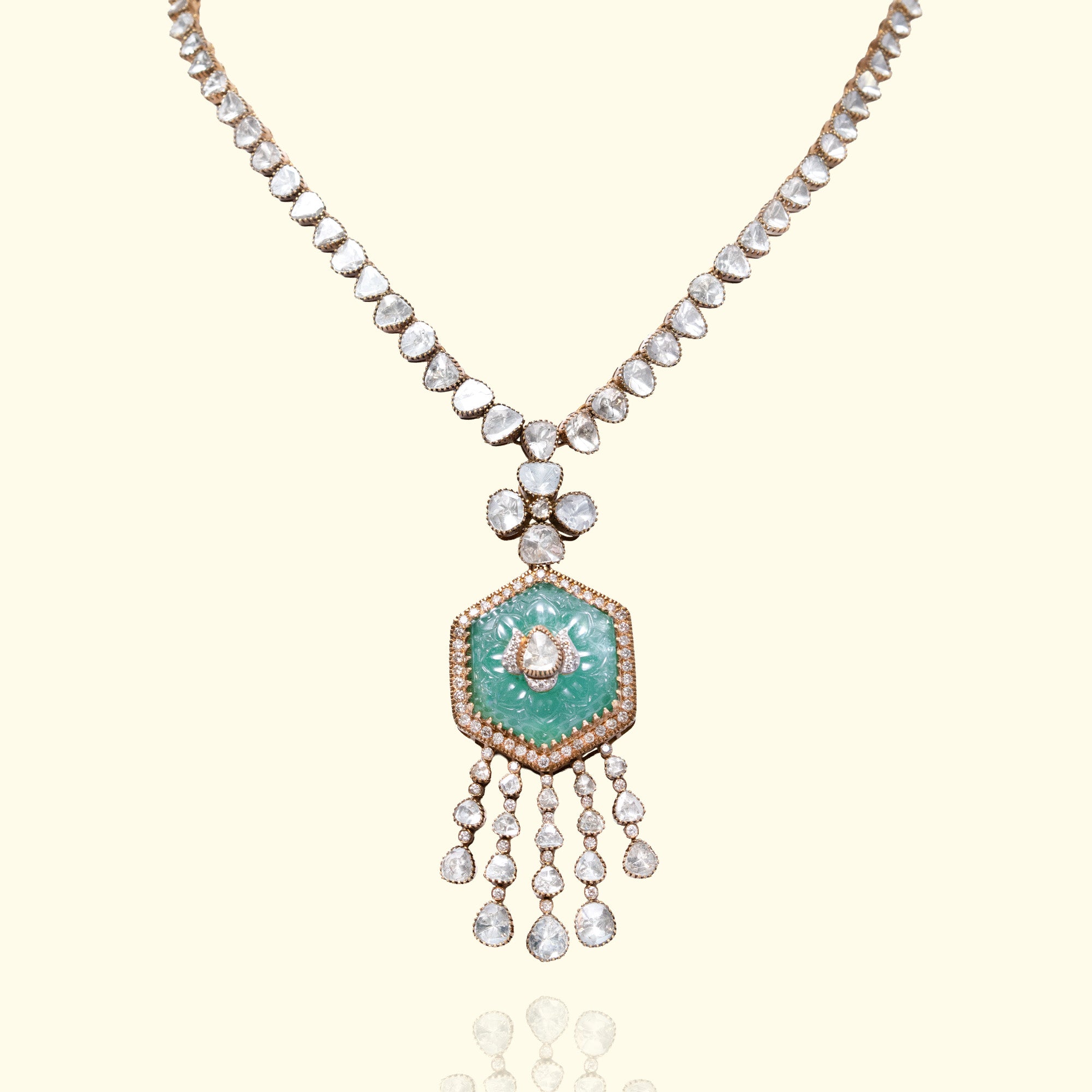 A gold necklace featuring a line of triangular polki diamonds leading to a large, hexagonal carved emerald pendant adorned with a central diamond motif and multiple cascading uncut diamond tassels.