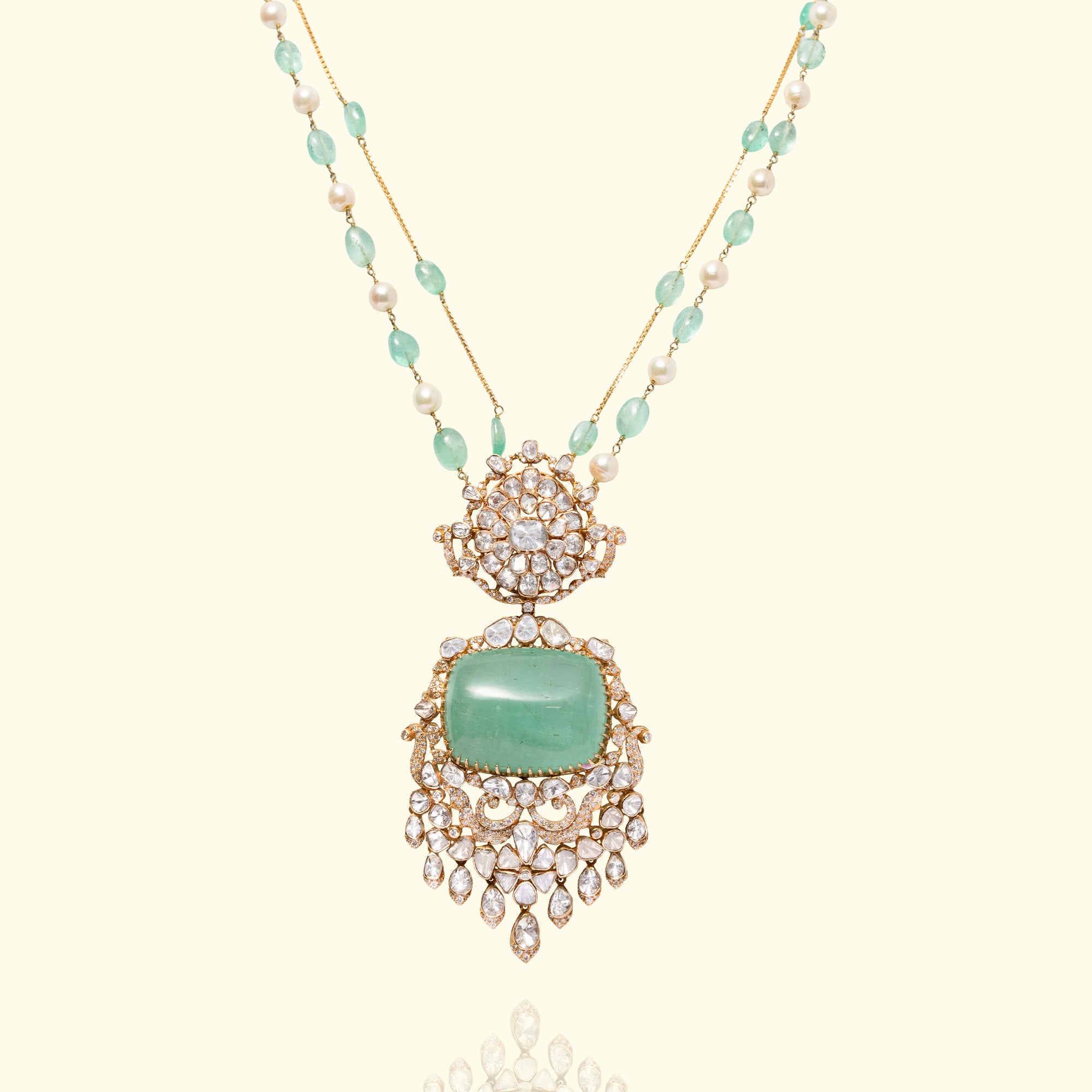 A regal gold necklace featuring a delicate chain of emerald beads and pearls, leadings to a massive, rectangular emerald cabochon pendant framed by ornate polki diamond scrollwork and cascading pear-shaped diamond drops.