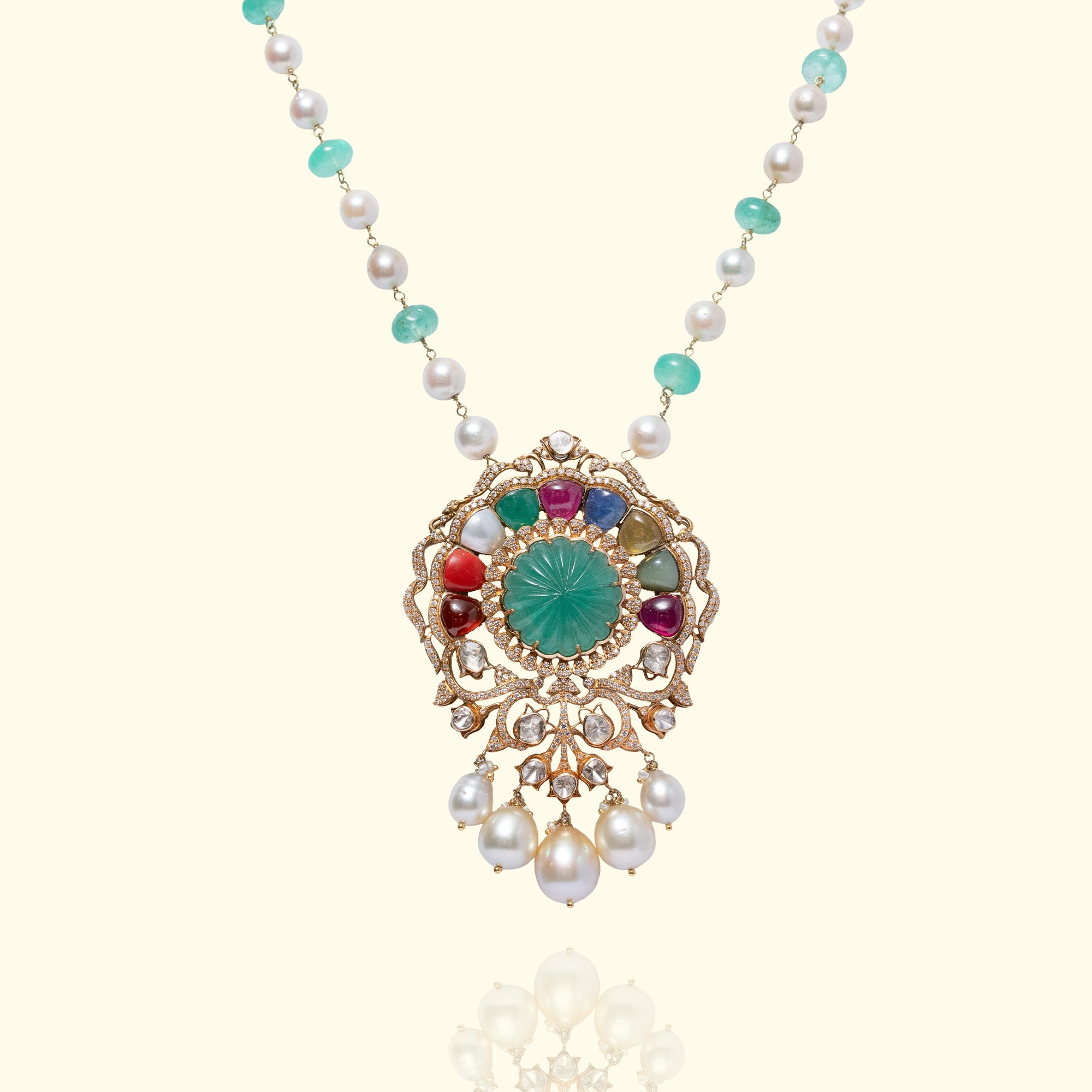 A magnificent gold polki navratan pendant featuring a central carved emerald surrounded by a rainbow of precious navratan milti-colored gemstones, uncut diamonds and dangling white South Sea pearls.