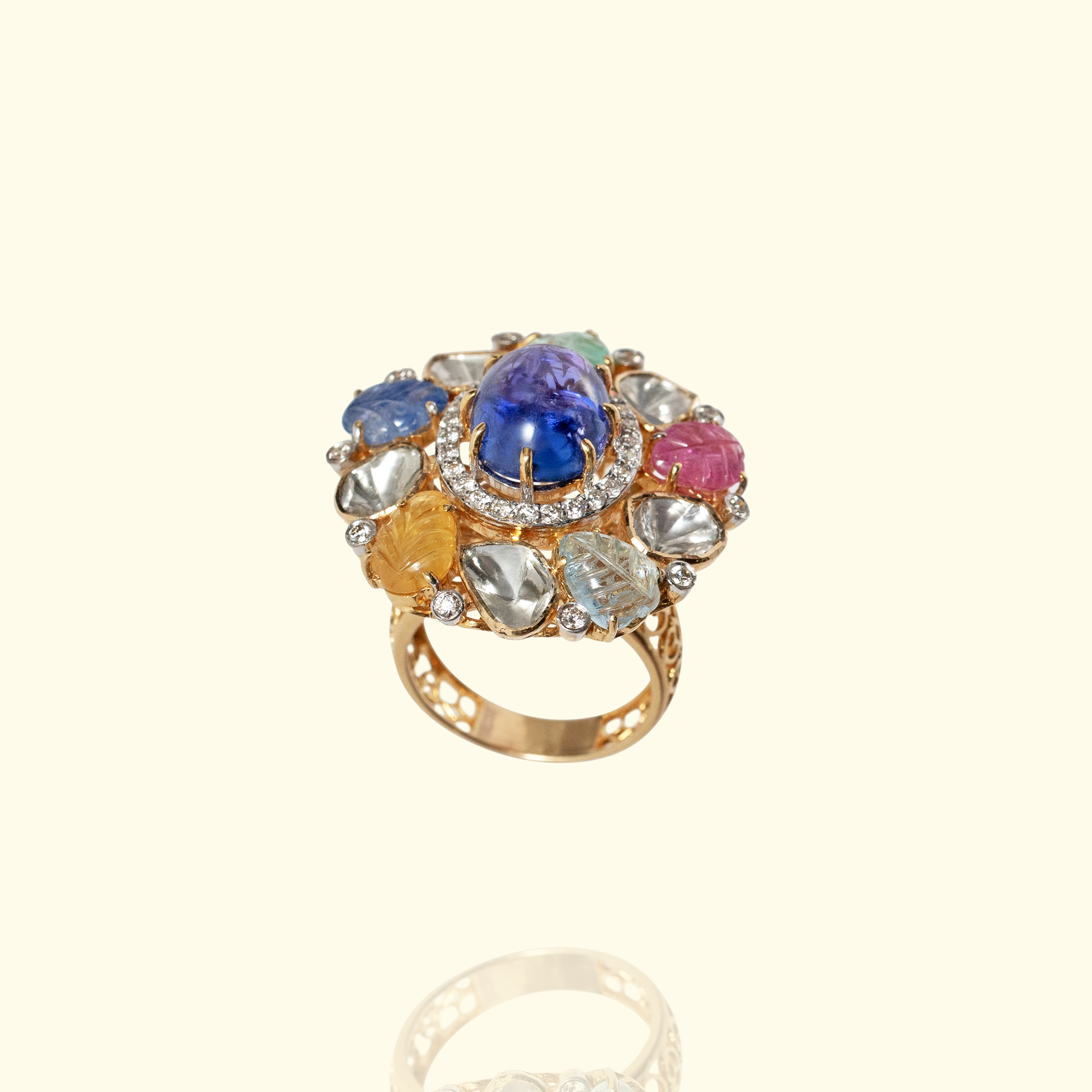 Luxurious gold Polki diamond cocktail ring centered with a large oval tanzanite cabochon, surrounded by carved multi-colored navratan gemstones including ruby and sapphire, emerald, tanzanite, yellow sapphire accented with a diamond-pave halo.