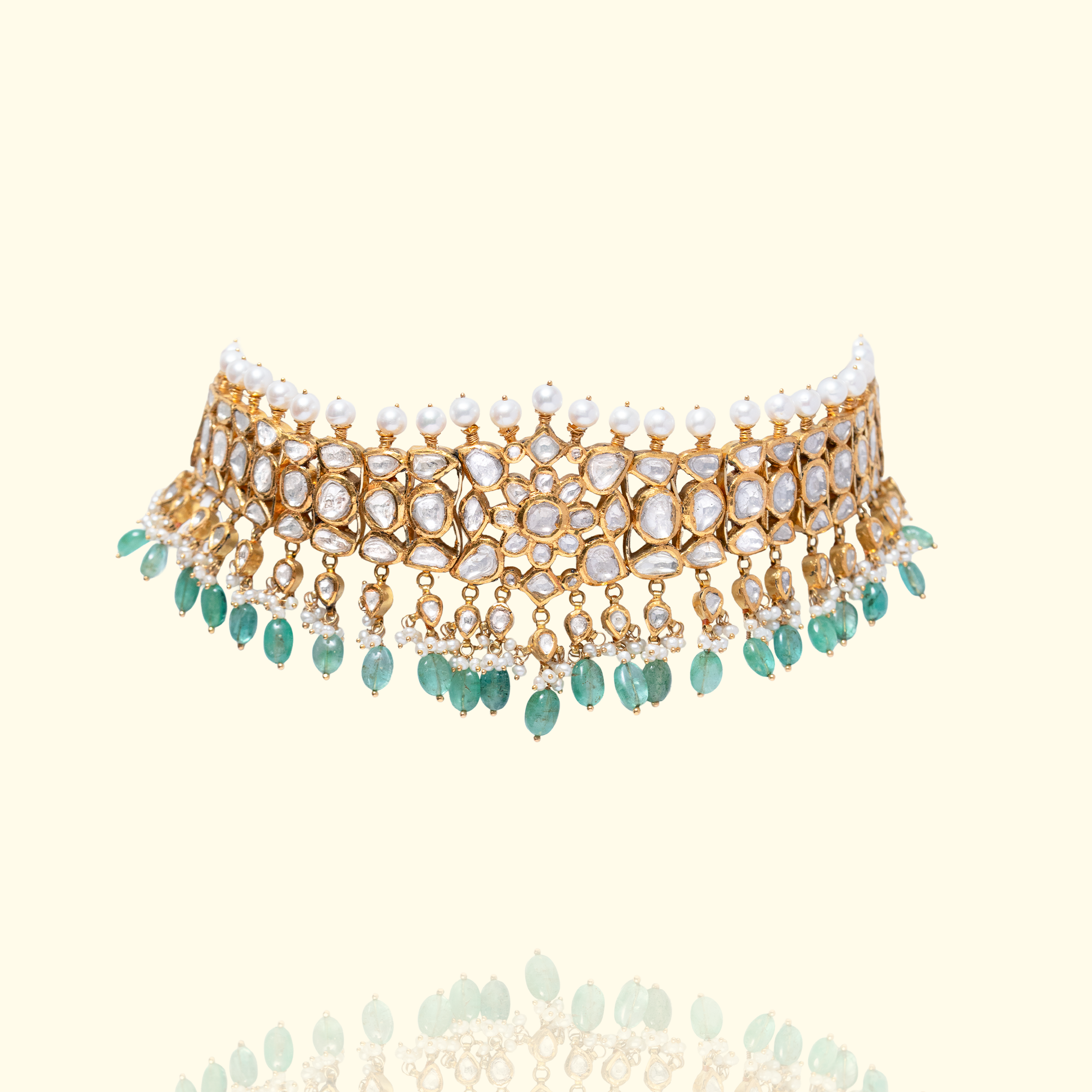 A magnificent high-glamour look featuring a pearl-strung polki choker layered with a wide, tiered gold bib necklace encrusted with teardrop polki diamonds and a lush emerald fringe.