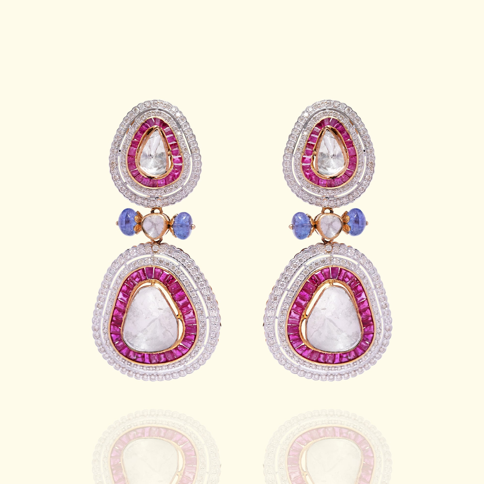 A pair of vibrant teardrop earrings featuring large triangular polki diamonds encased in ruby baguettes and shimmering pavé halos, accented with delicate blue sapphire beads.