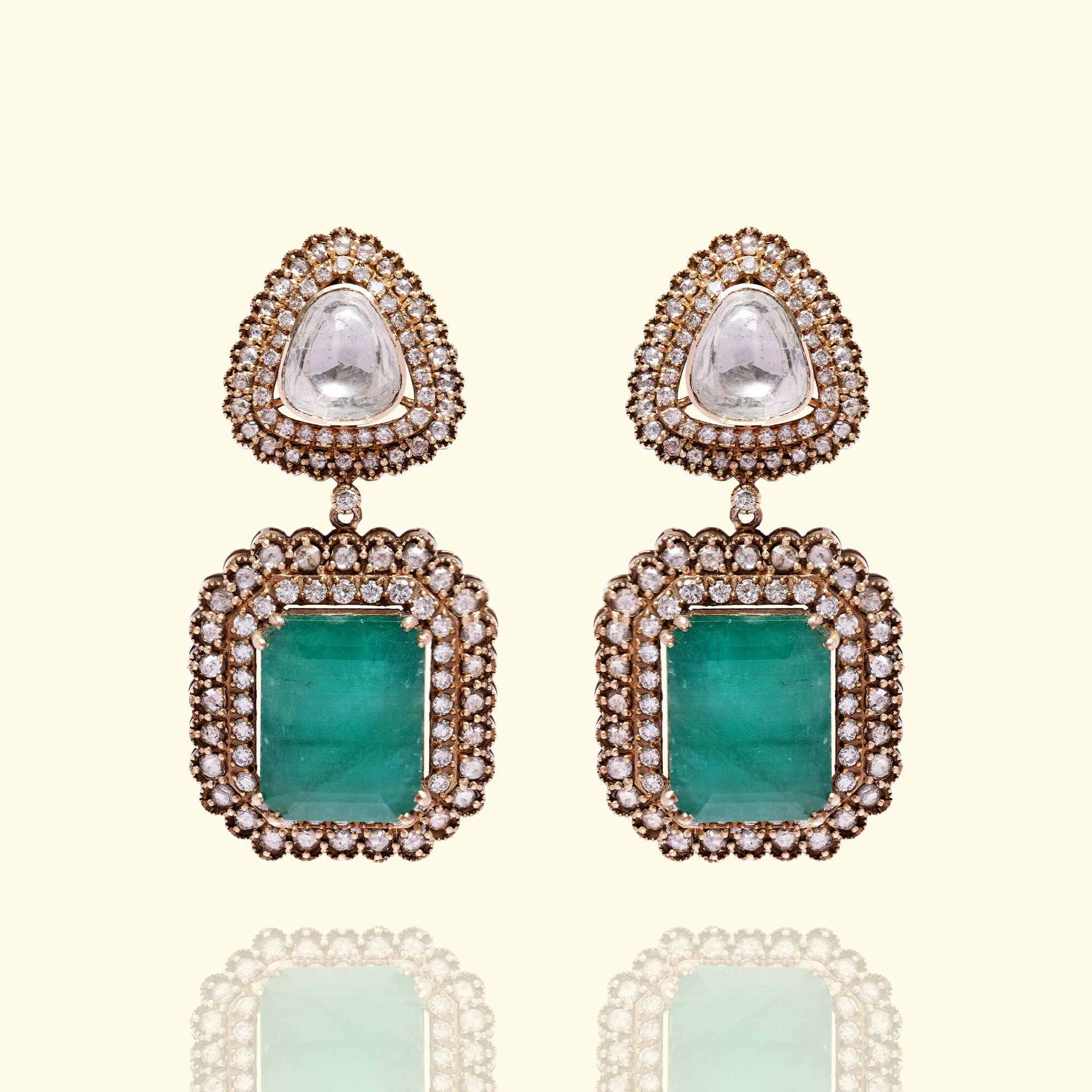 An elegant double-drop earrings featuring a pear-shaped polki diamond stud and a large, rectangular emerald-cut emerald, both framed by shimmering pavé diamond halos.