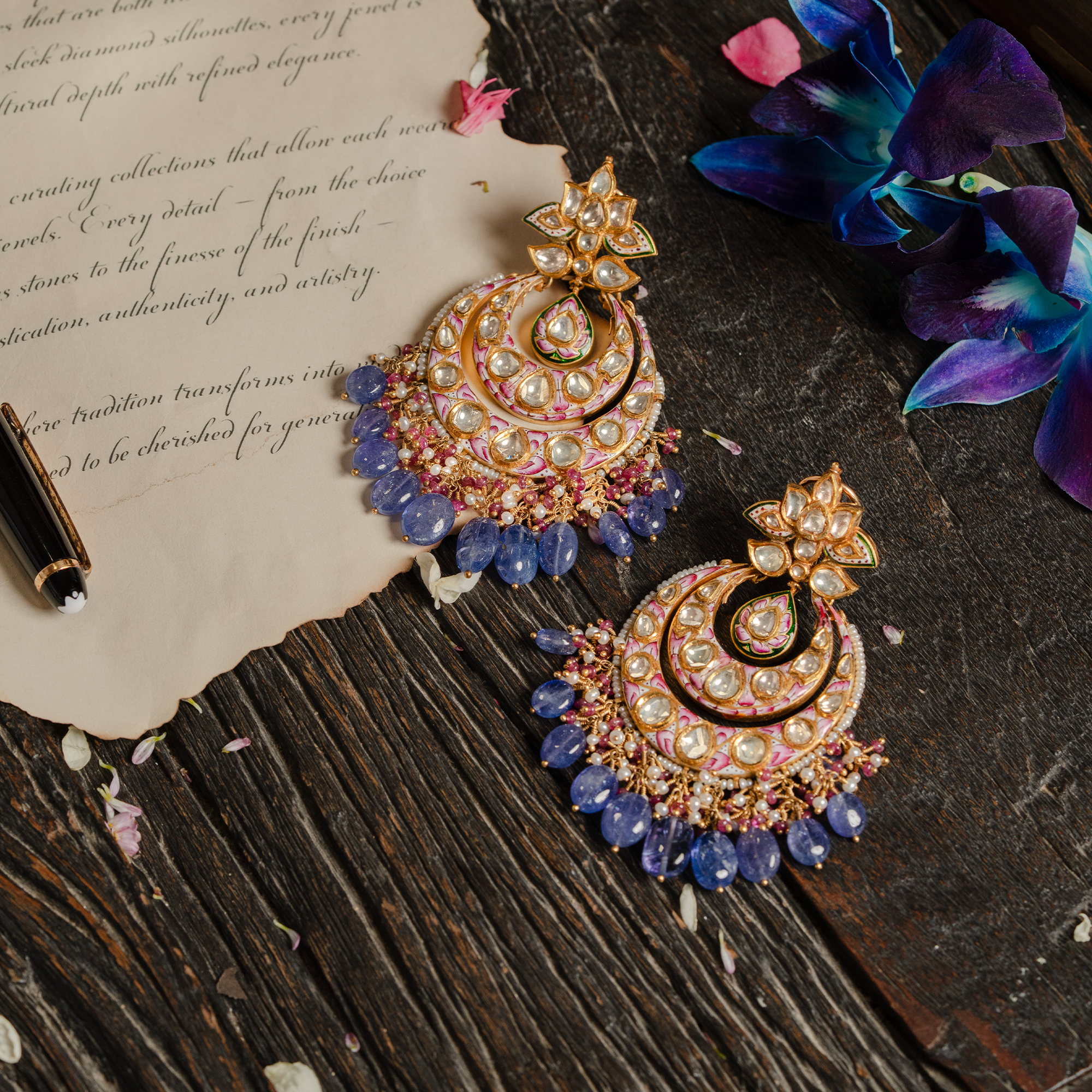 A pair of ornate gold polki crescent-shaped earrings featuring pink and white floral meenakari enamel work and uncut diamond settings, finished with a lush fringe of tanzanite bead drops and japanese freshwater pearls.