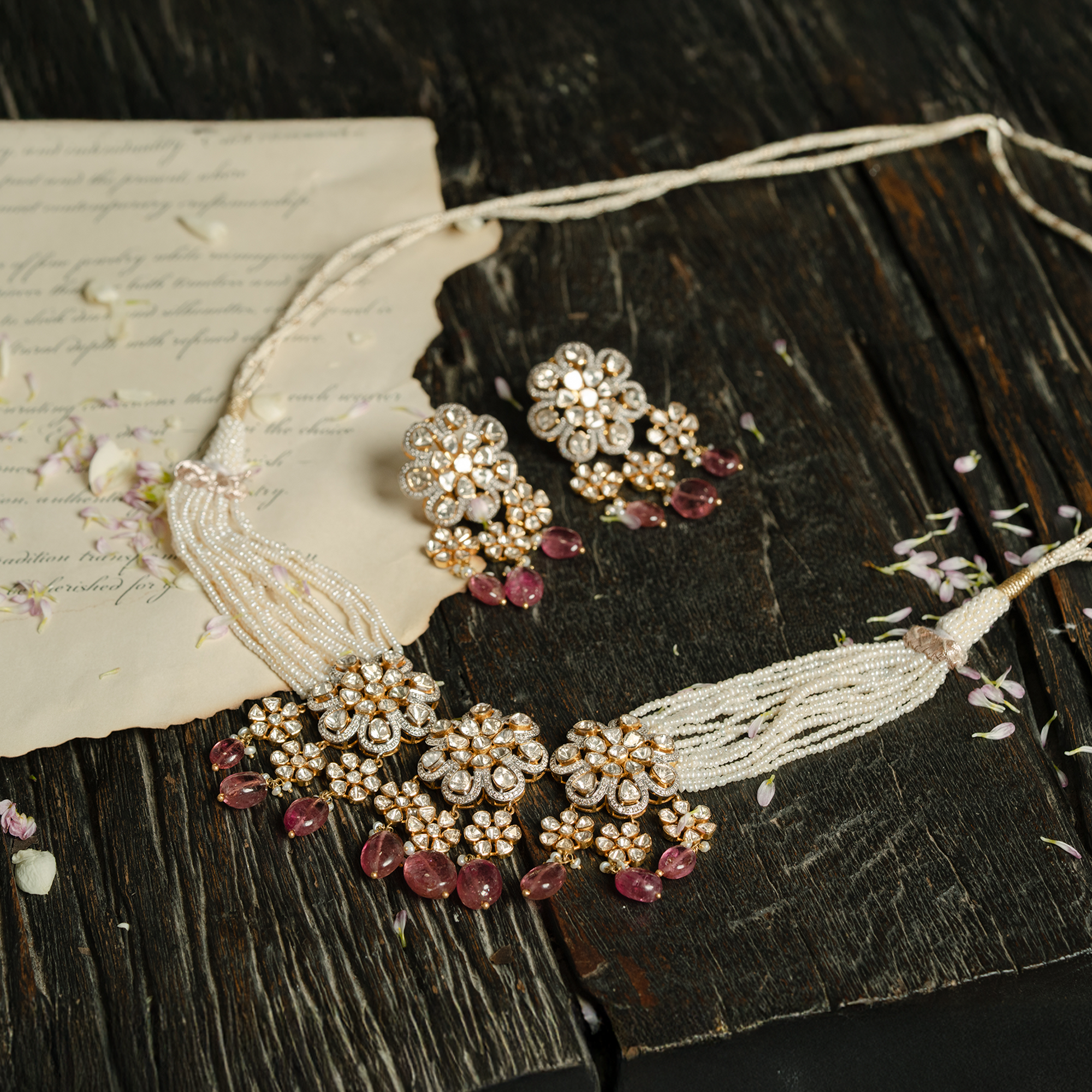 A coordinated jewelry set featuring a multi-strand seed pearl necklace and matching earrings, both adorned with floral-motif polki diamond pendants and hanging ruby drops.