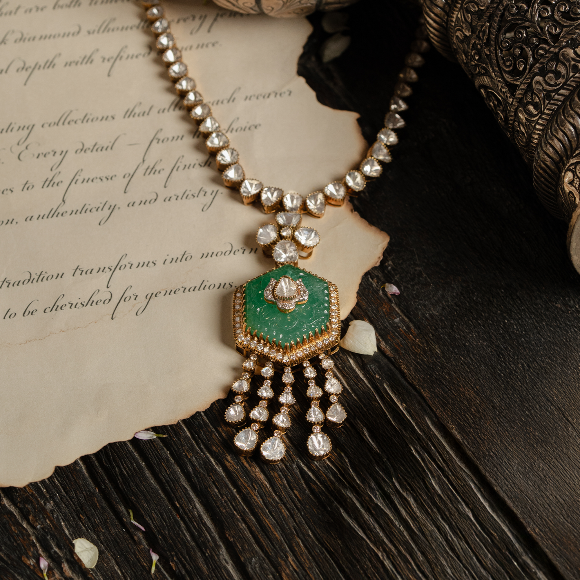A gold necklace featuring a line of triangular polki diamonds leading to a large, hexagonal carved emerald pendant adorned with a central diamond motif and multiple cascading uncut diamond tassels.
