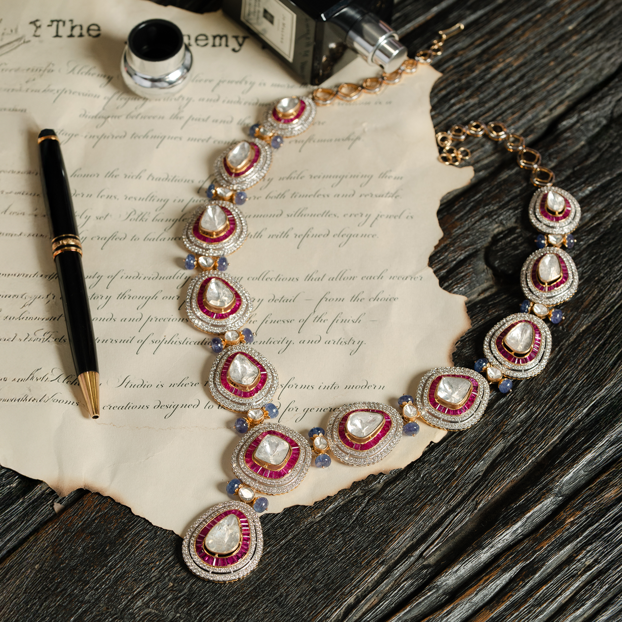 Gold Polki diamond collar necklace featuring graduated pear-shaped uncut diamonds surrounded by vibrant ruby halos and blue sapphire accents on vintage parchment.